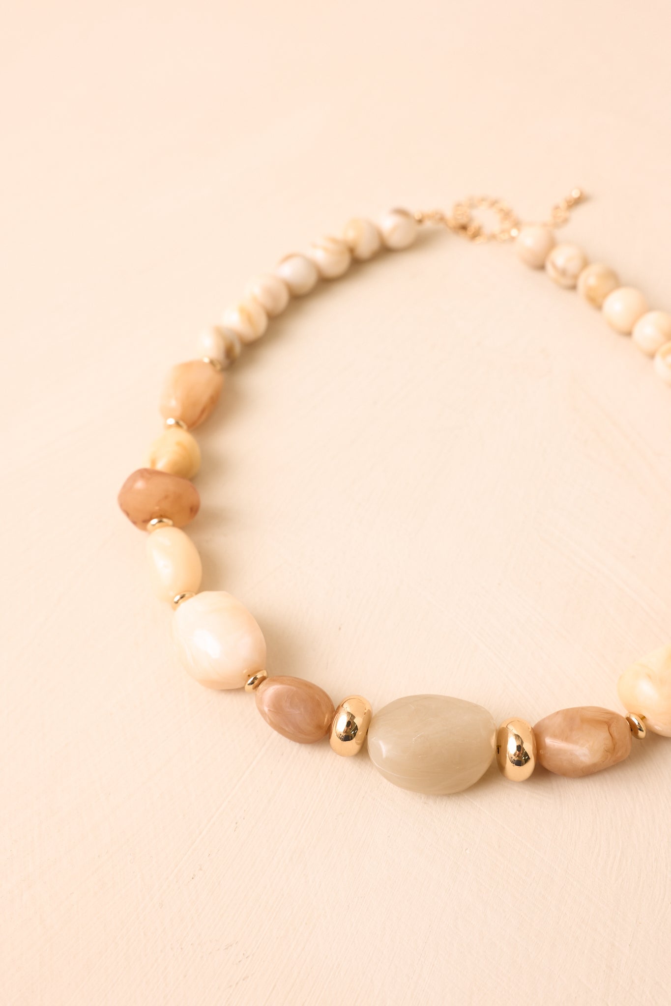 Mixed neutral bead necklace against a beige background featuring organic bead shapes, polished spacers, and softly blended earthy tones.