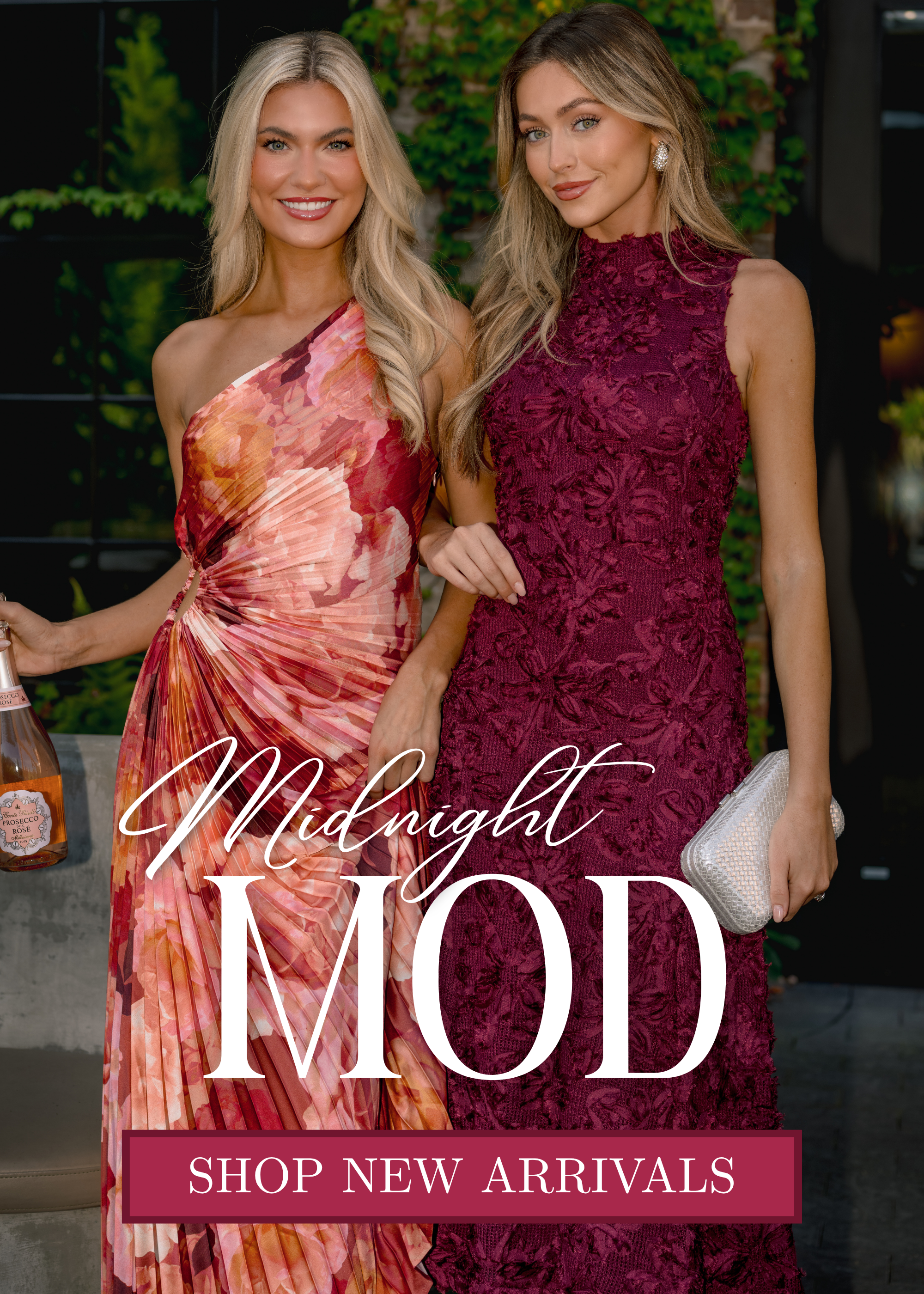 Two women wearing elegant evening dresses, one in a floral one-shoulder dress and the other in a burgundy textured dress, standing outdoors at night. Text reads “Midnight Mod” and “Shop New Arrivals.”