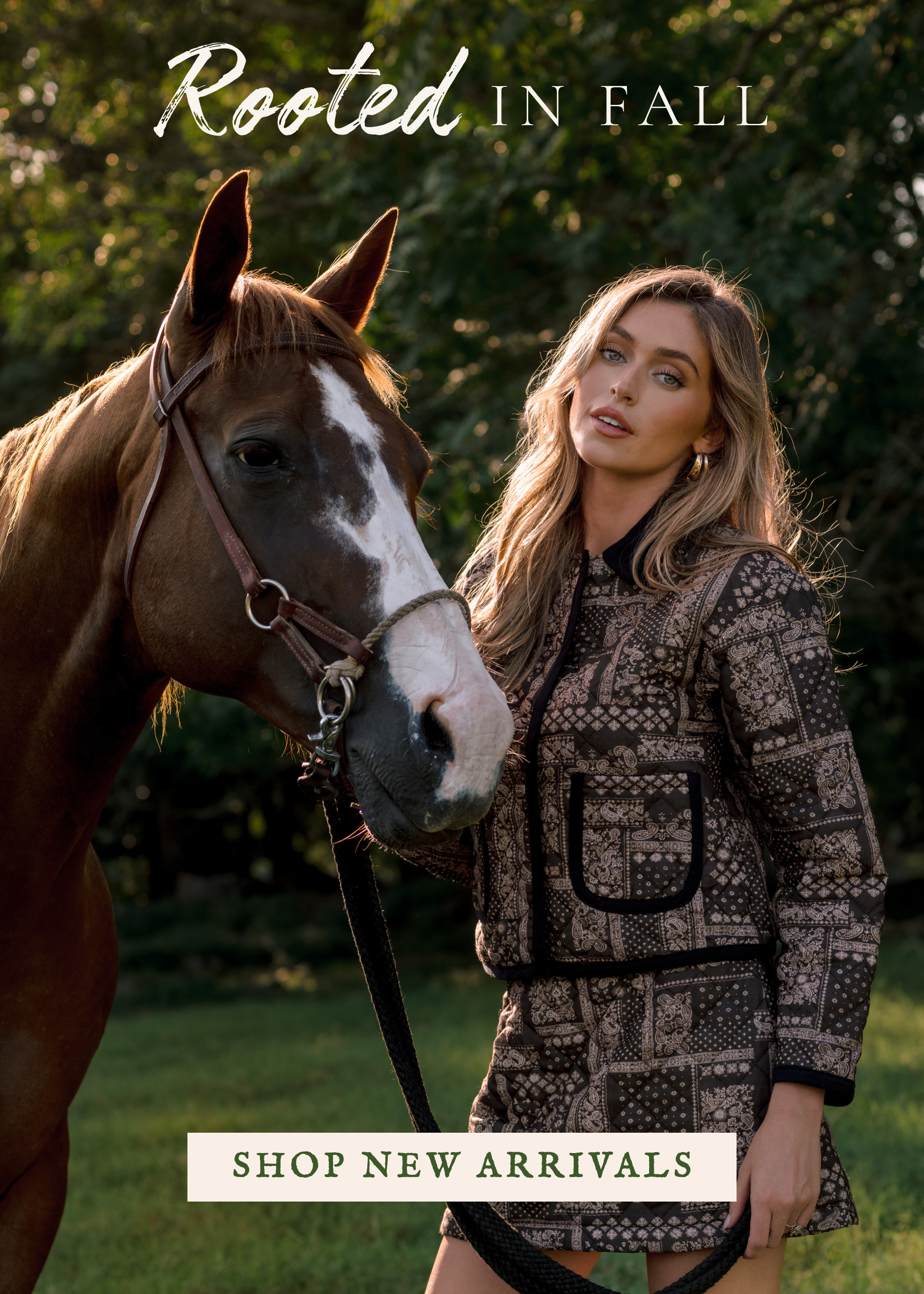 Model wearing a patterned jacket and shorts stands beside a horse in a wooded field, with text reading “Rooted in Fall” and “Shop New Arrivals.”