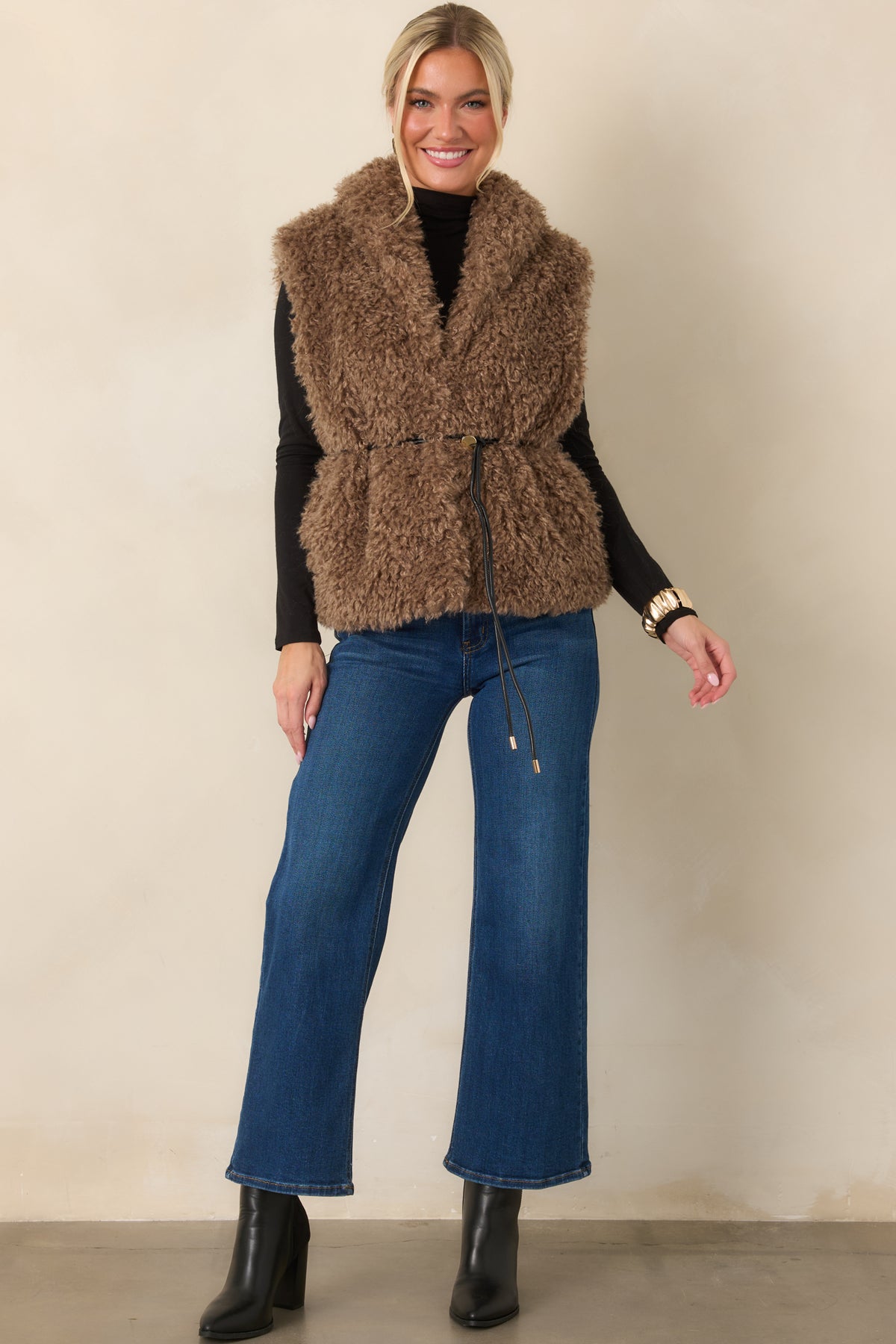 Warm mocha vest showcasing plush curly faux fur, functional pockets, and a softly structured hip-length shape.
