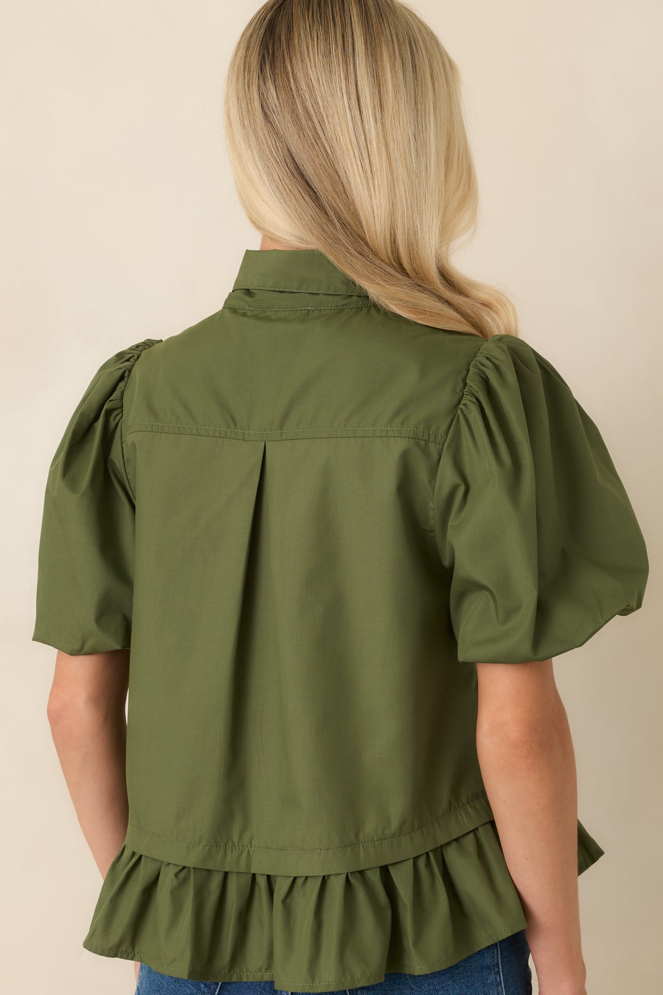 Moss green blouse showing the back of the feminine silhouette with voluminous puff sleeves and a softly flared peplum hem.