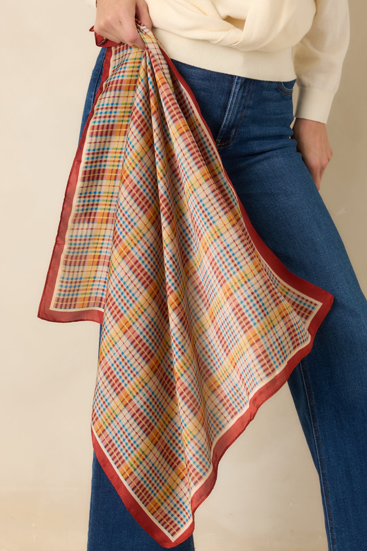 Multicolor plaid scarf displays intersecting blue, golden yellow, and rust lines across an ivory background with a bold rust edge.