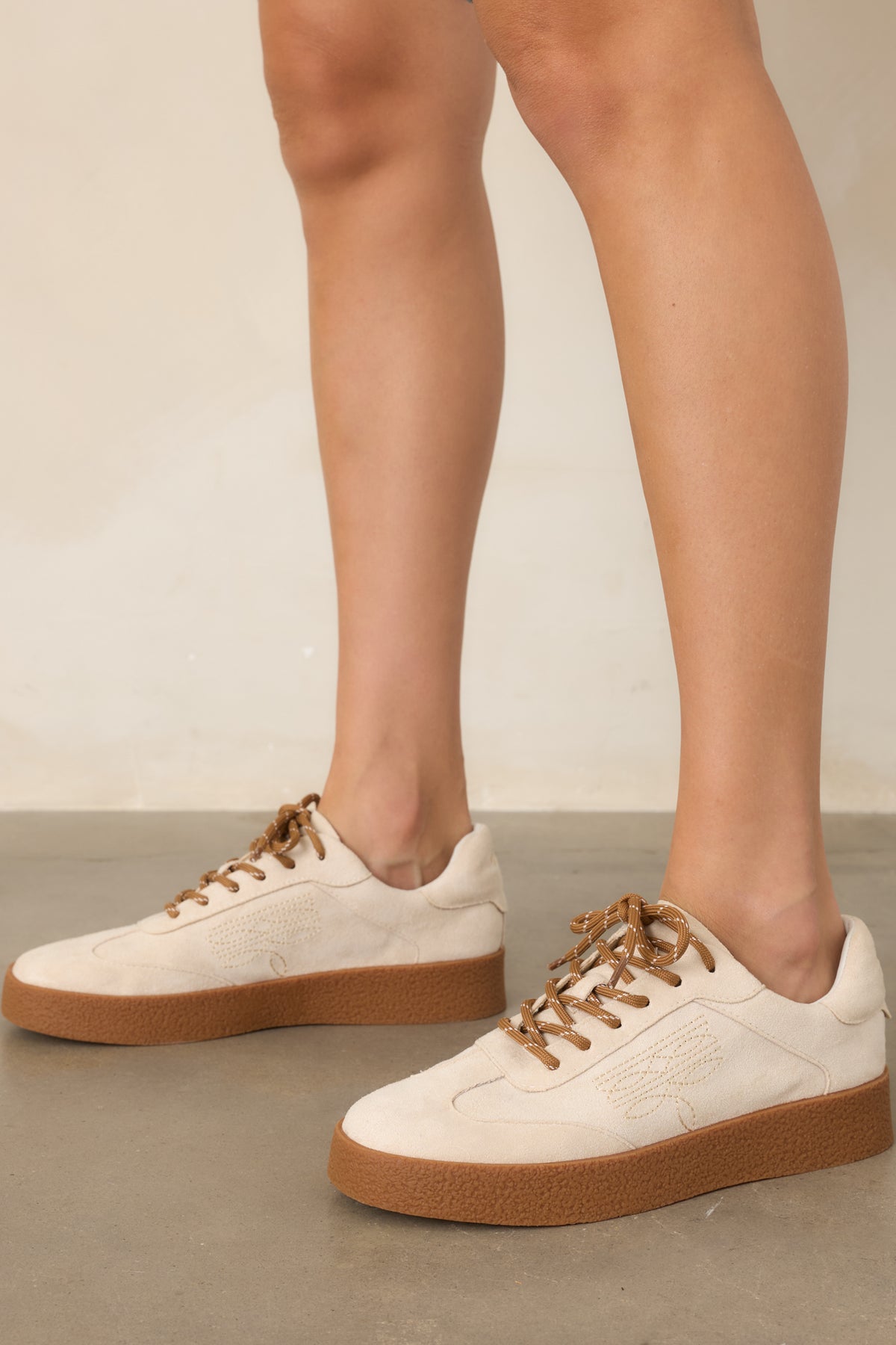 Natural faux suede lace-up sneakers showcasing decorative stitching along the sides.