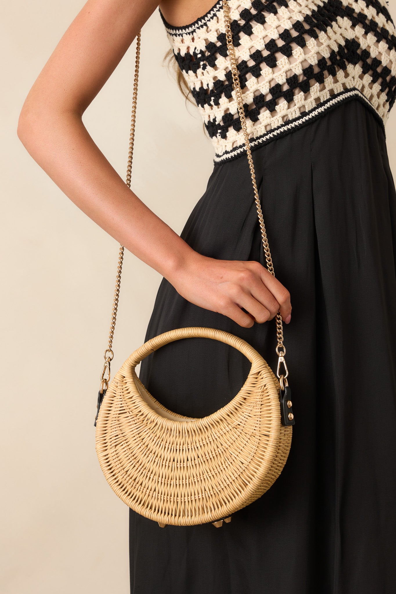 Natural rattan handbag with black faux leather accents and structured shape, displayed with gold crossbody chain draped at the side.