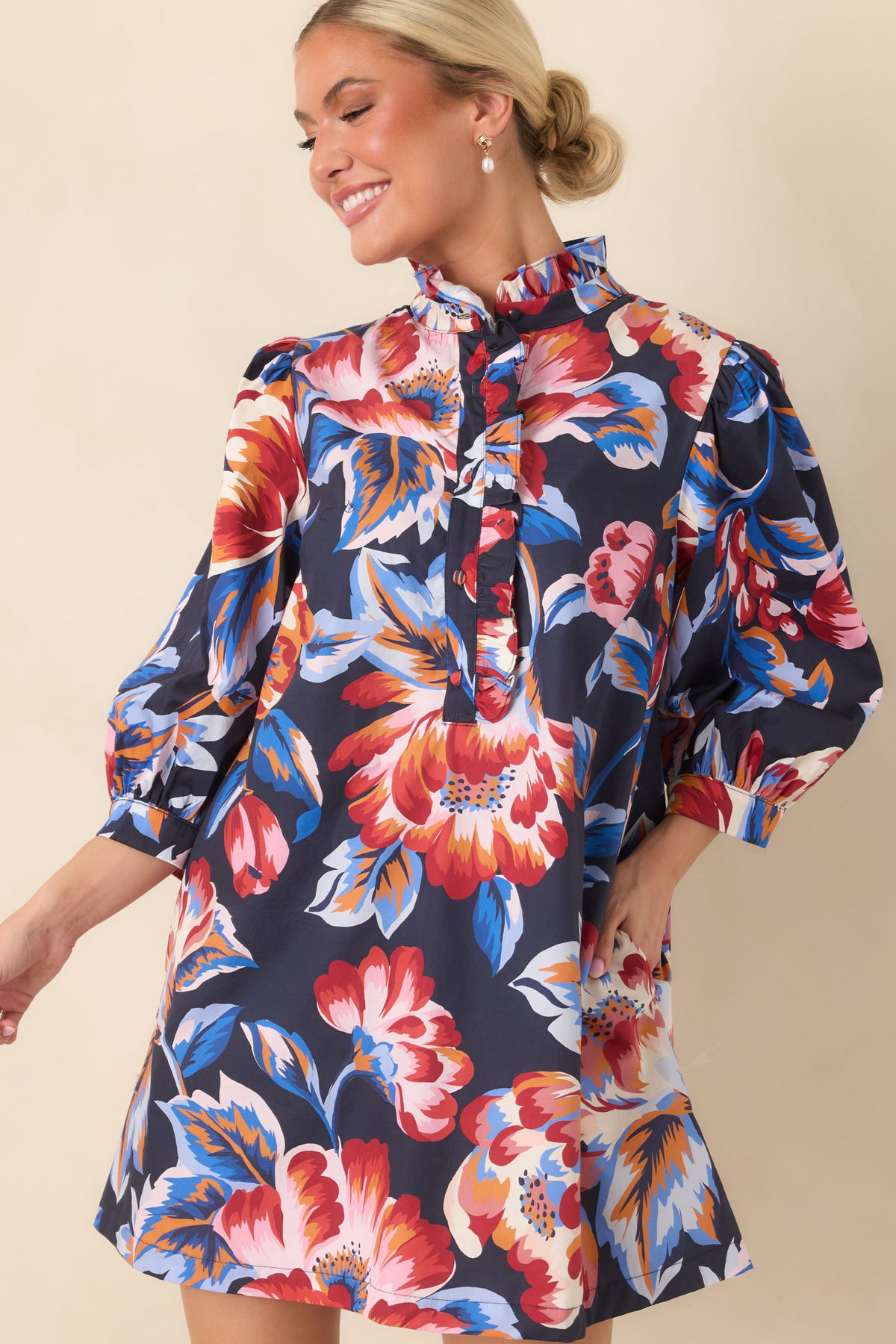 Navy floral mini dress featuring a ruffled high neckline, partial button-front closure, and colorful oversized floral print.