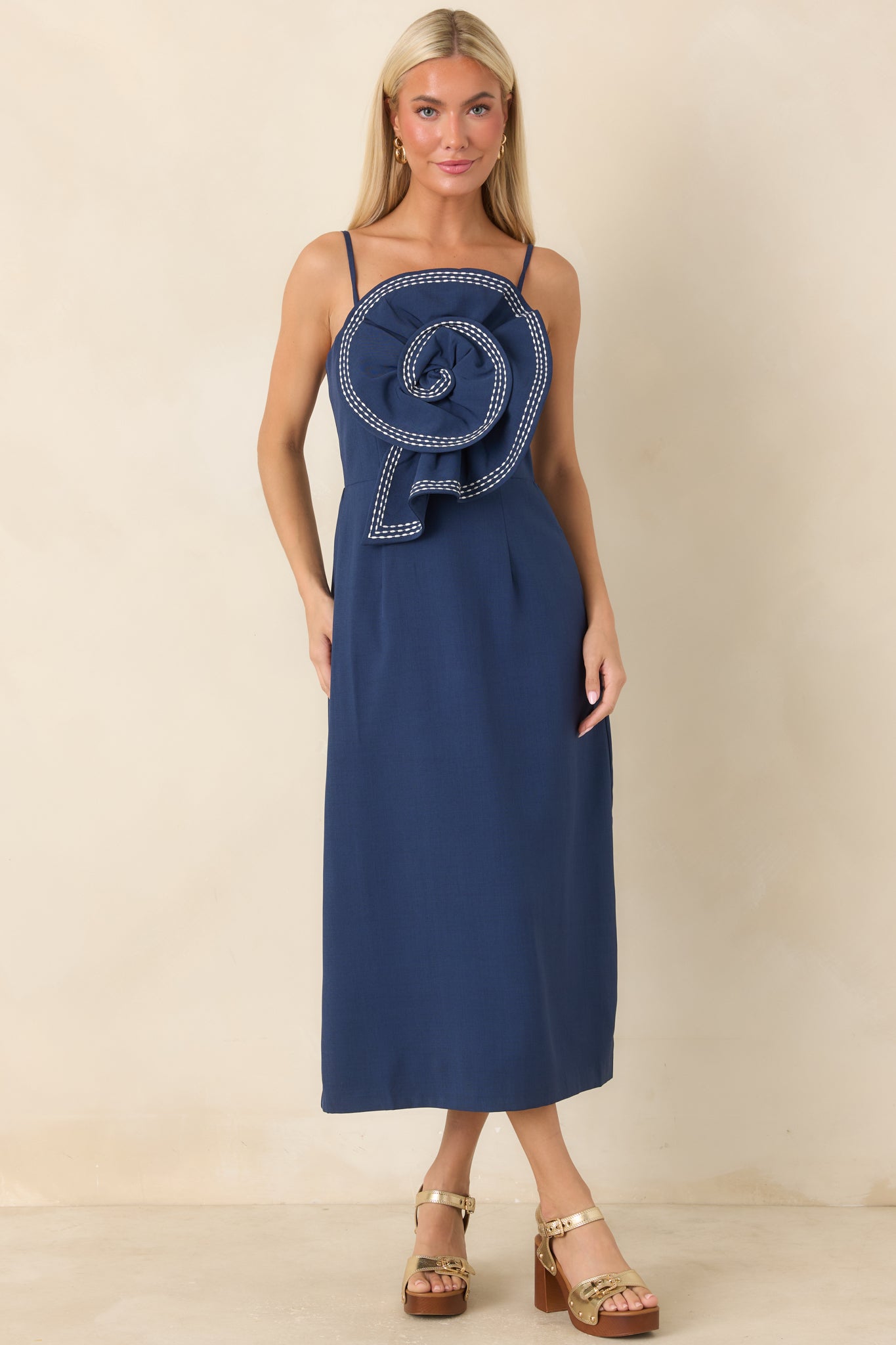 Navy midi dress featuring slim adjustable straps, a fitted bodice, and an oversized sculptural rosette across the front.