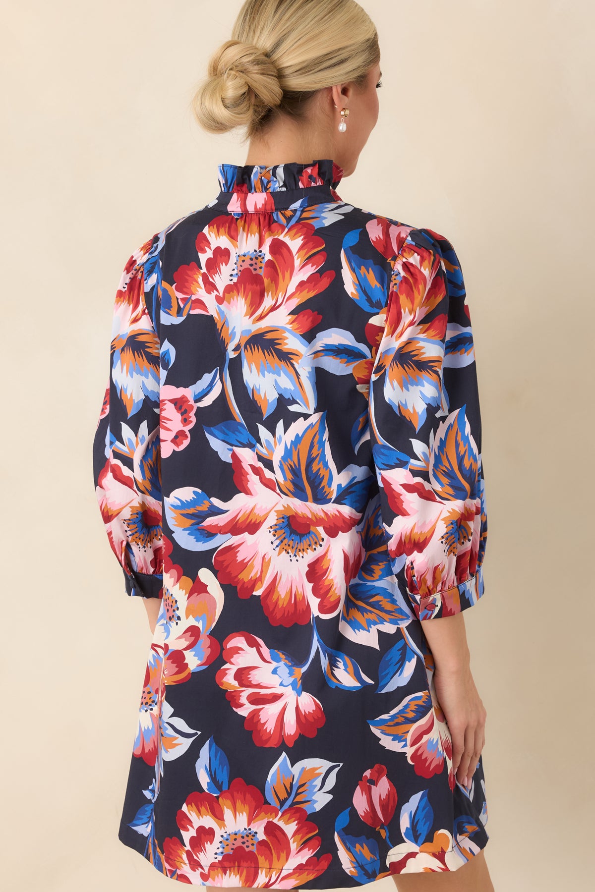Back view of navy floral mini dress featuring a ruffled high neckline, gathered back detail, and colorful oversized floral print.