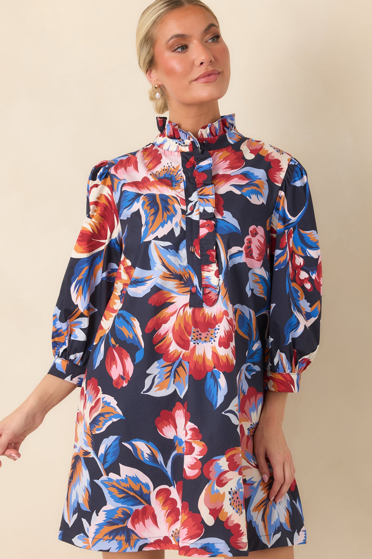 Navy floral mini dress featuring a ruffled high neckline, partial button placket, and vibrant red, pink, orange, and blue flowers.