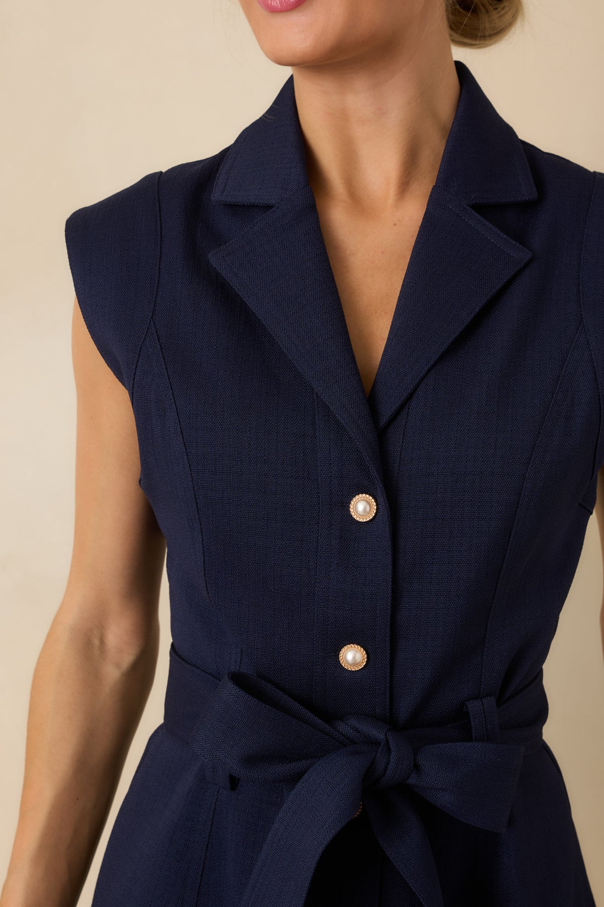 Close-up of navy woven mini dress featuring a notched collar, V-neckline, princess seams, and gold-accented pearl buttons.