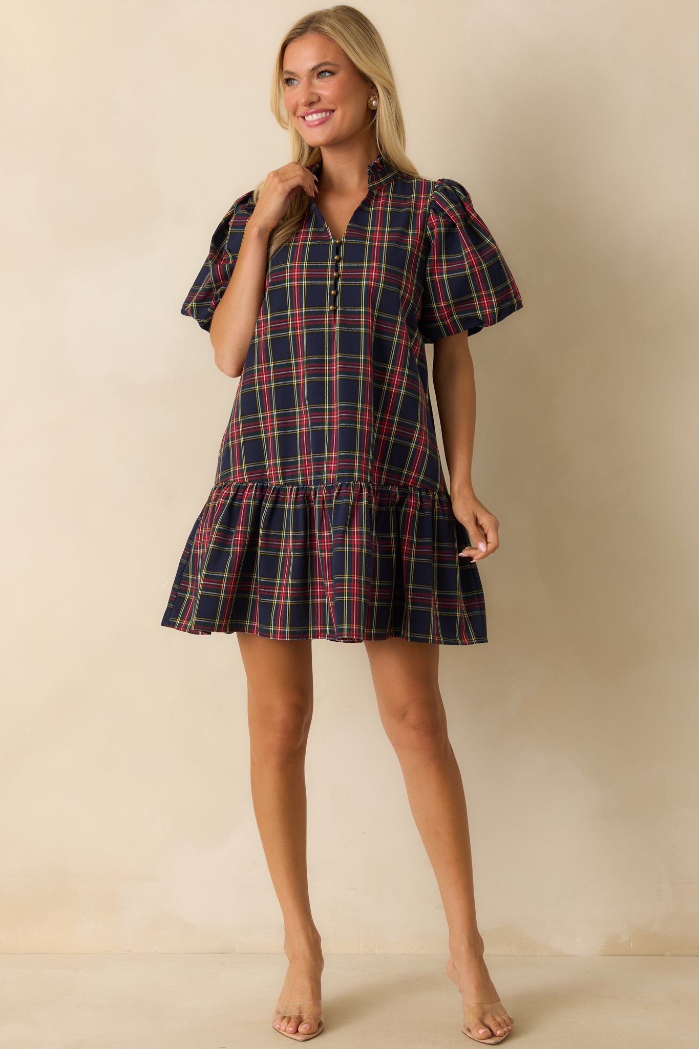 Navy plaid mini dress with short puff sleeves, split neckline with button detail, ruffled drop hem, and side pockets.