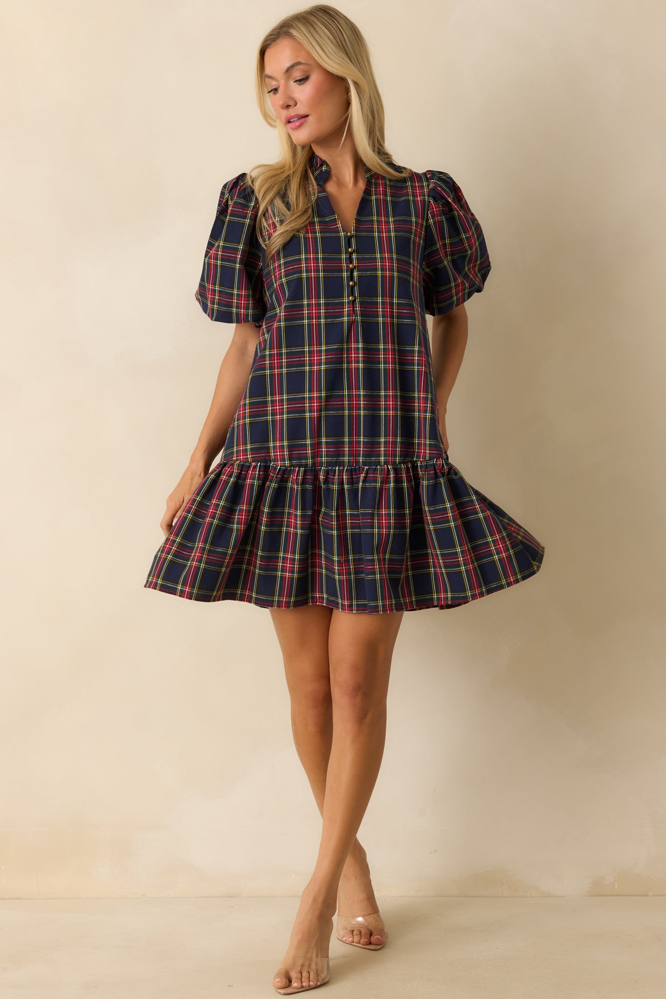 Mini dress in navy plaid highlighting split neckline with buttons, side pockets, and flowing ruffled drop hem.