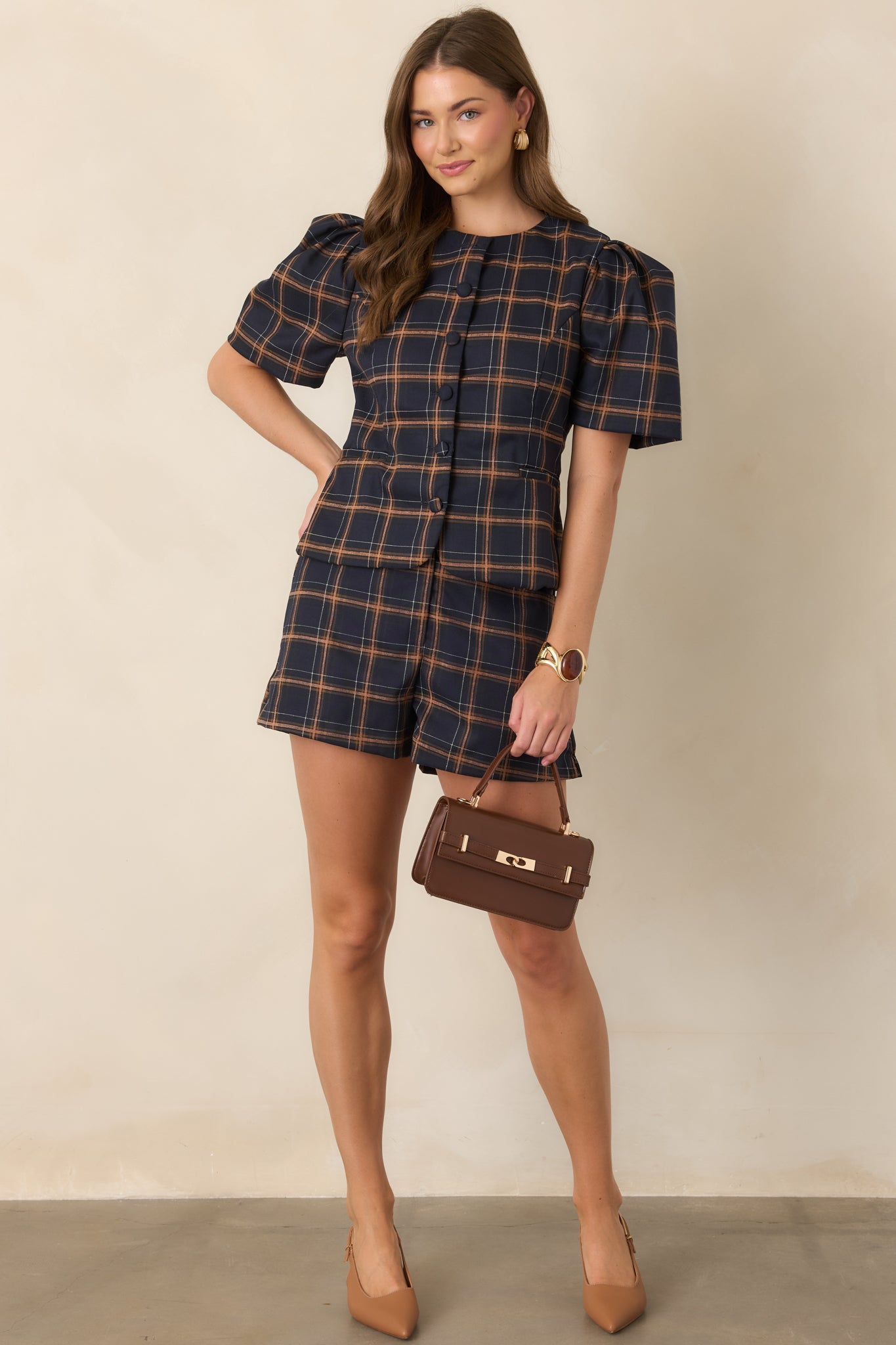 Fitted plaid top showcasing a navy base with camel and ivory checks, a classic round neckline, rounded elbow-length sleeves, and fabric-covered buttons down the front.