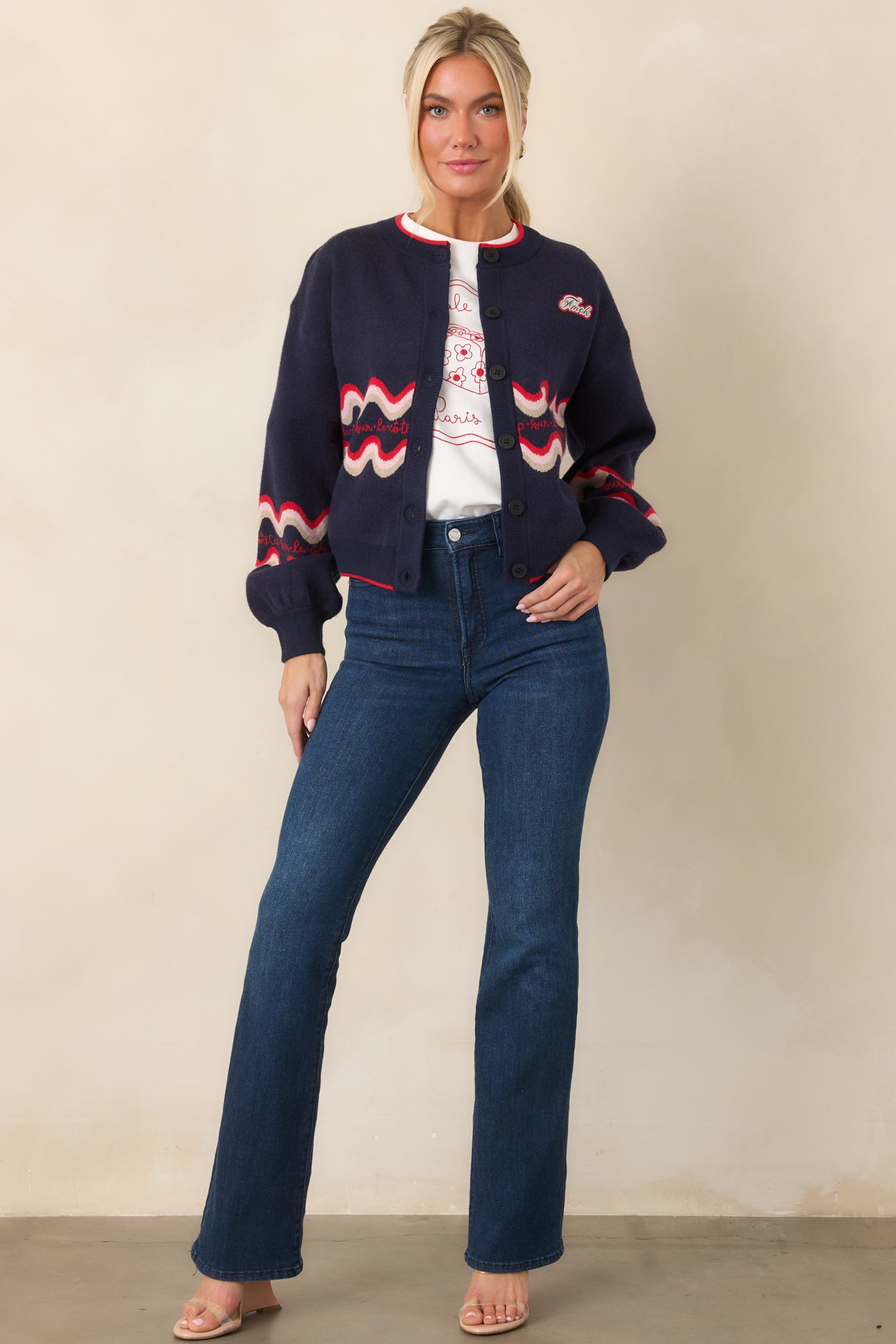 Deep navy knit cardigan featuring red and cream wave detailing across the body and long sleeves, contrast red trim, and a small chest logo patch.