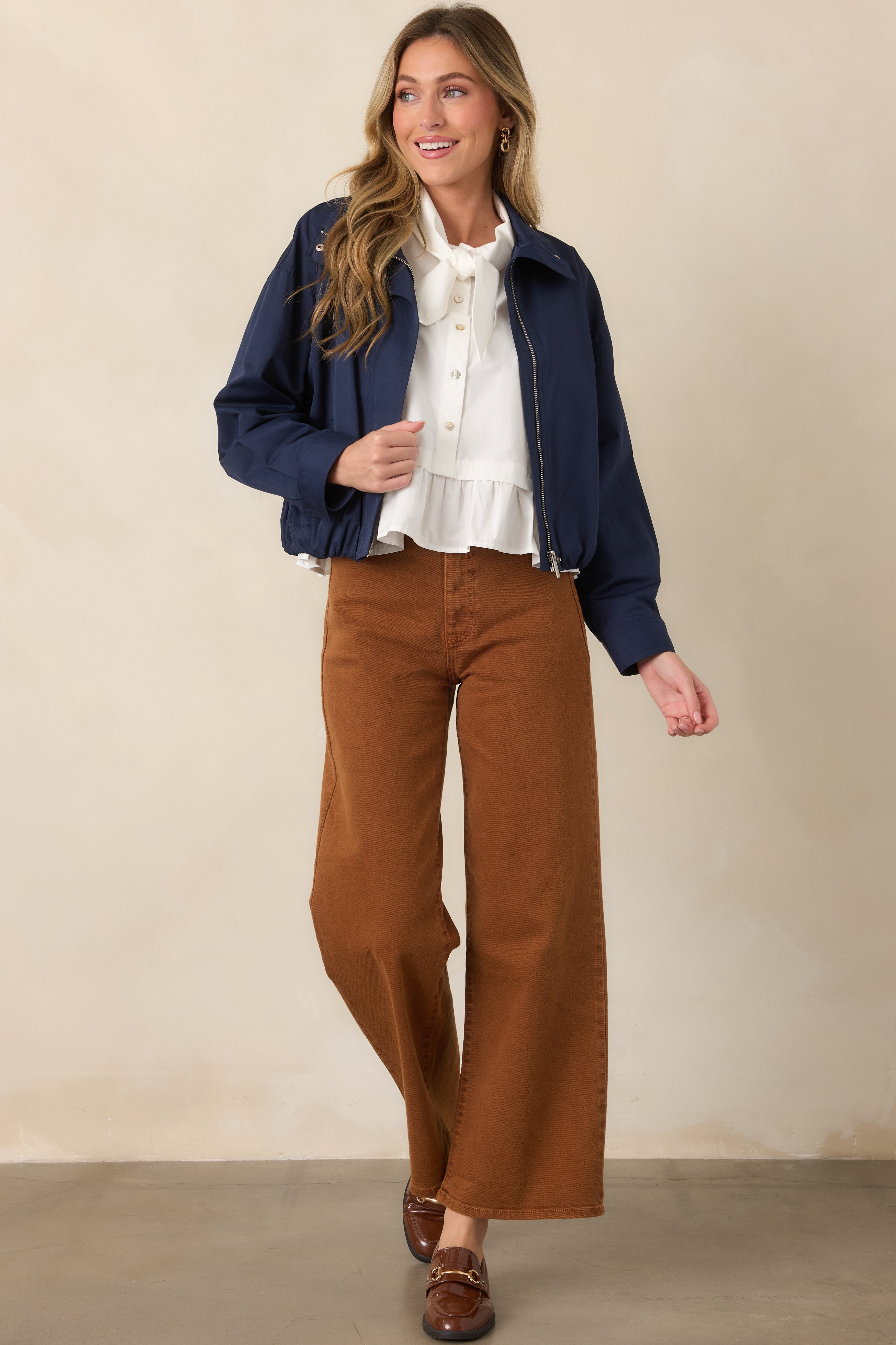 Navy bomber jacket showcasing its relaxed cropped silhouette, smooth woven shell, dropped shoulders, and long sleeves with button cuffs.