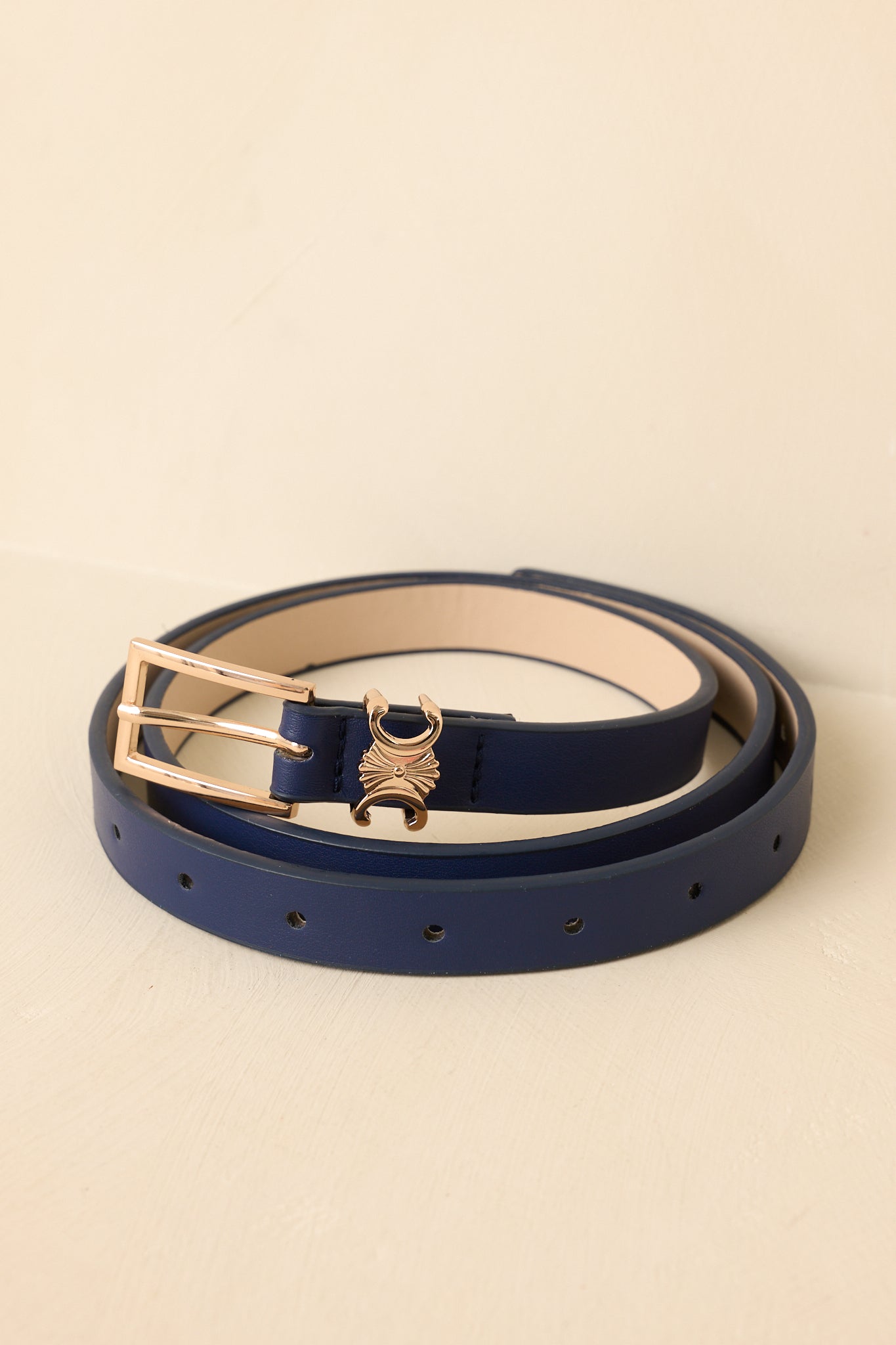 Cropped view of navy slim faux leather belt featuring a narrow silhouette and gold-tone buckle.