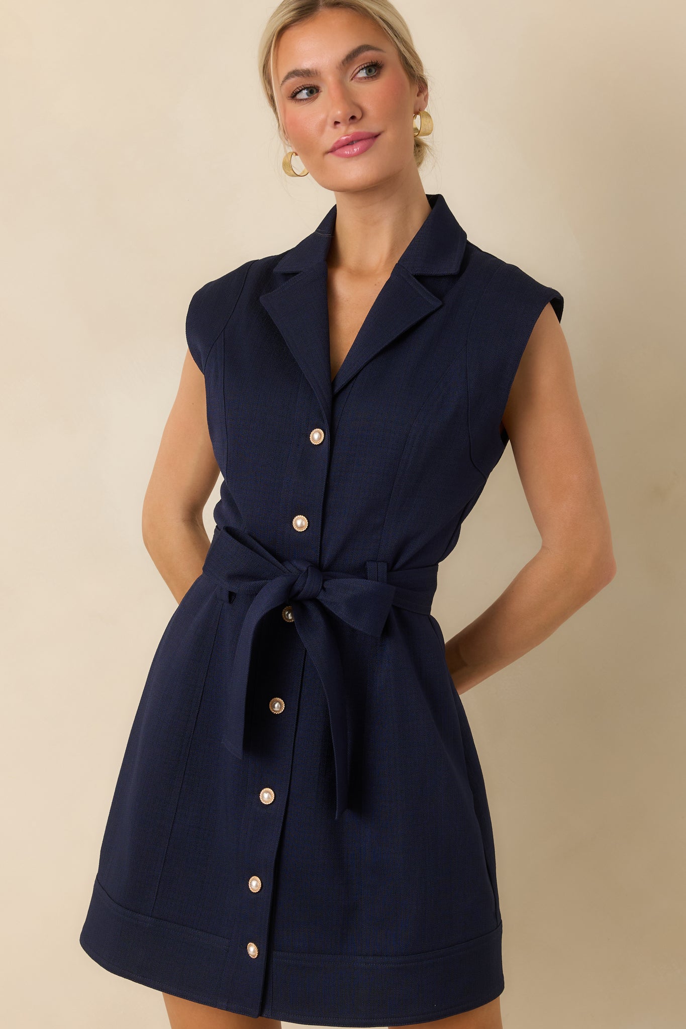 Structured navy mini dress with a V-neck notched collar, cap sleeves, tied waist, functional buttons, and banded hem.