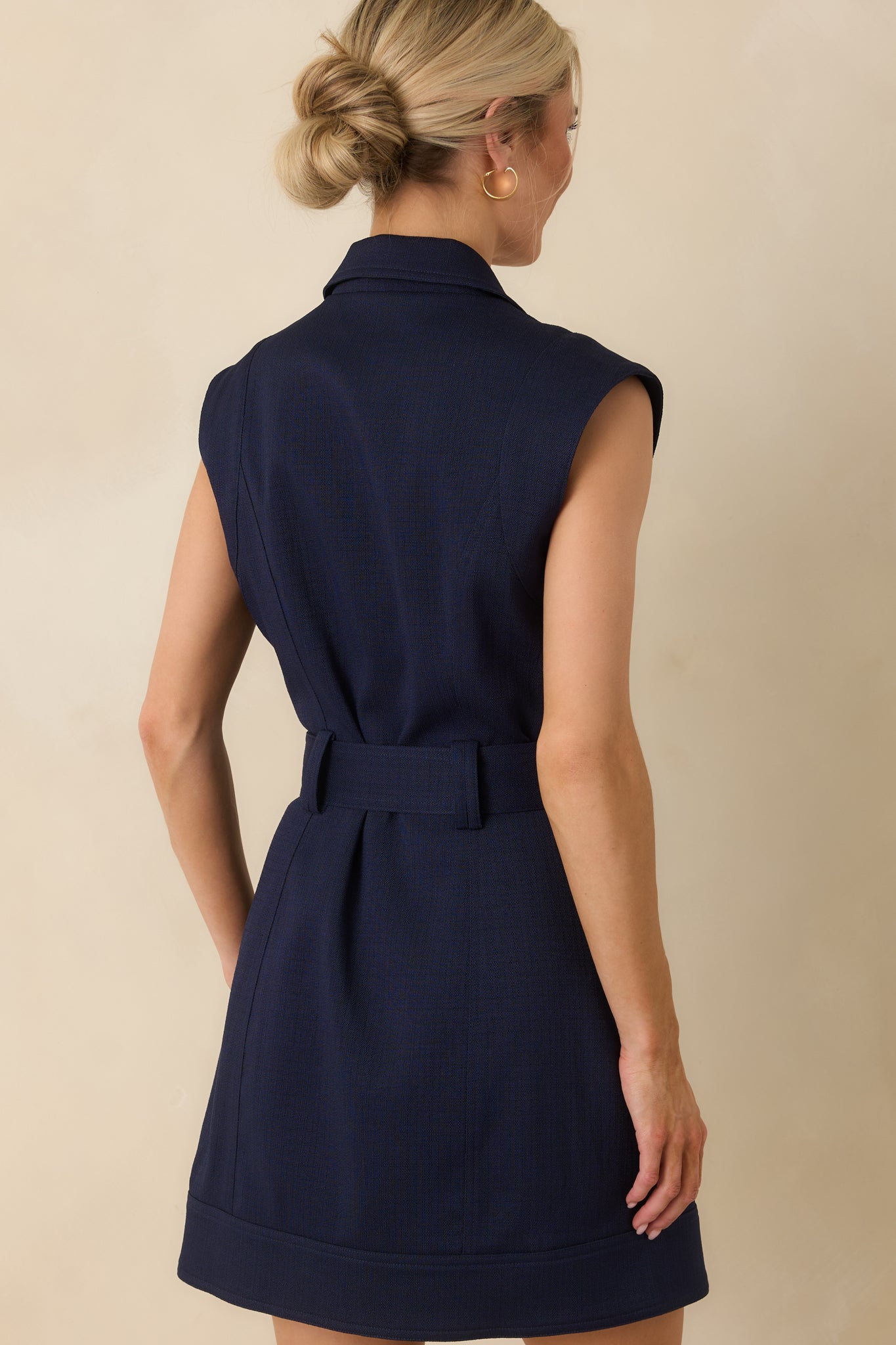 Back view of navy mini dress showcasing structured cap sleeves, a fitted seamed bodice, belted waist, and A-line silhouette.