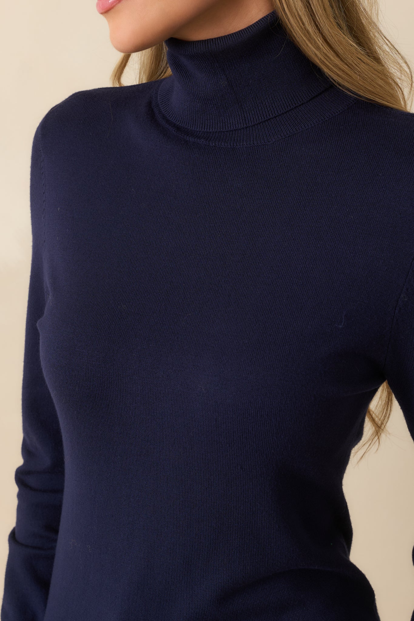 Close-up of navy sweater showing soft knit fabric, ribbed cuffs, tapered hem, and turtle neckline.