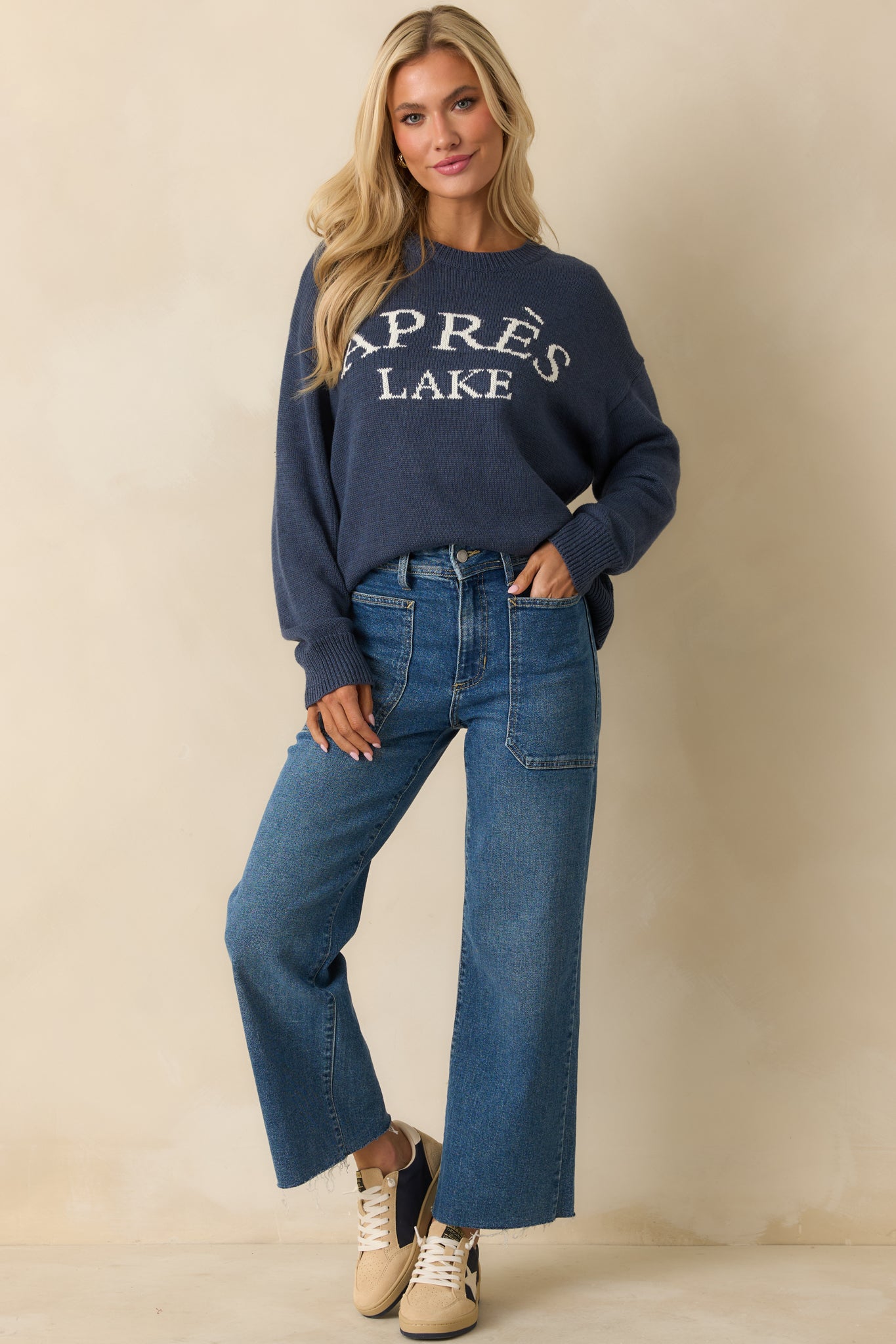 Full body shot highlighting the relaxed fit of the navy sweater with ribbed trim and bold front lettering.
