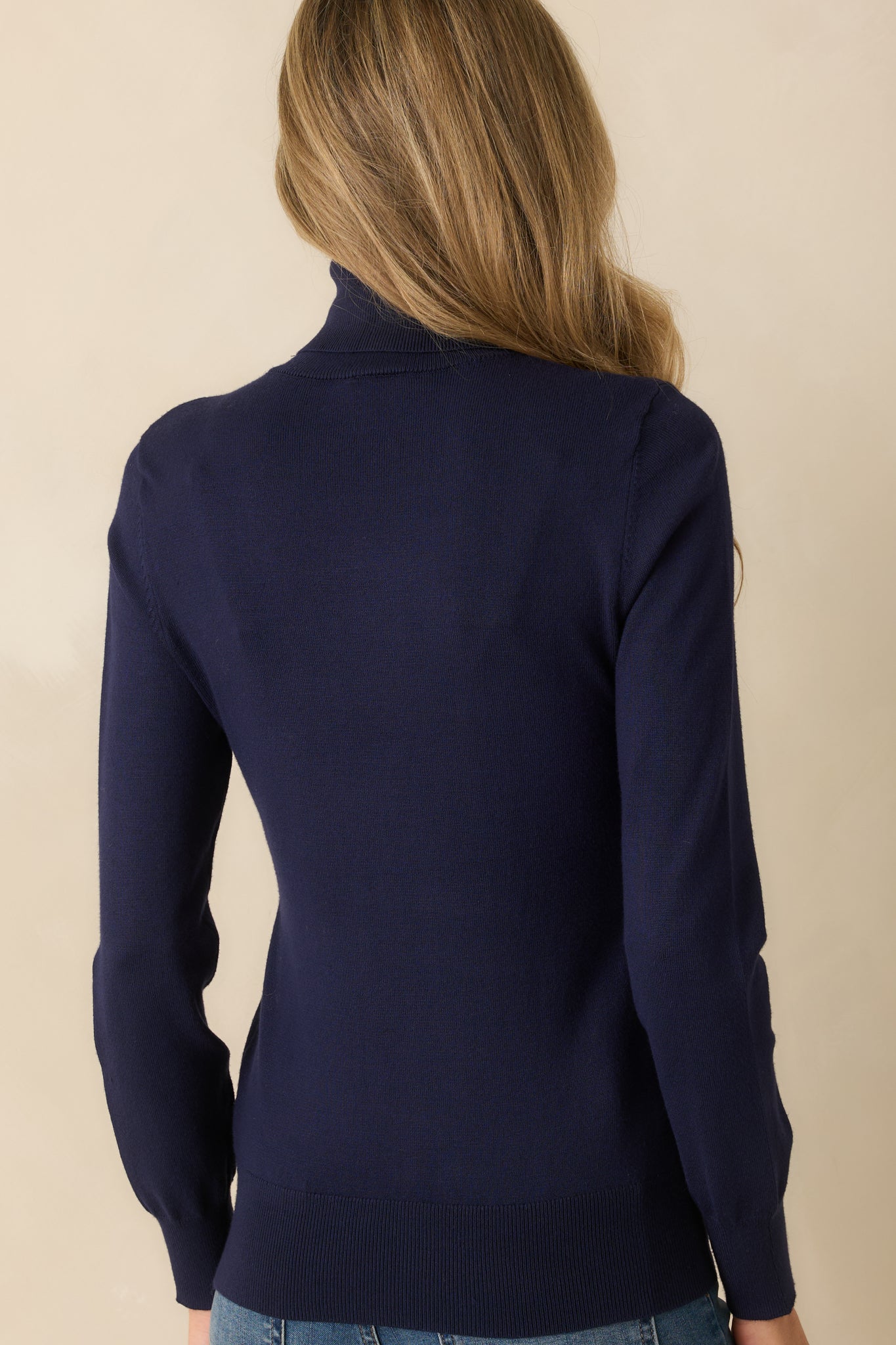 Rear view of navy sweater displaying long sleeves, ribbed cuffs, tapered bottom hem, and smooth knit texture.
