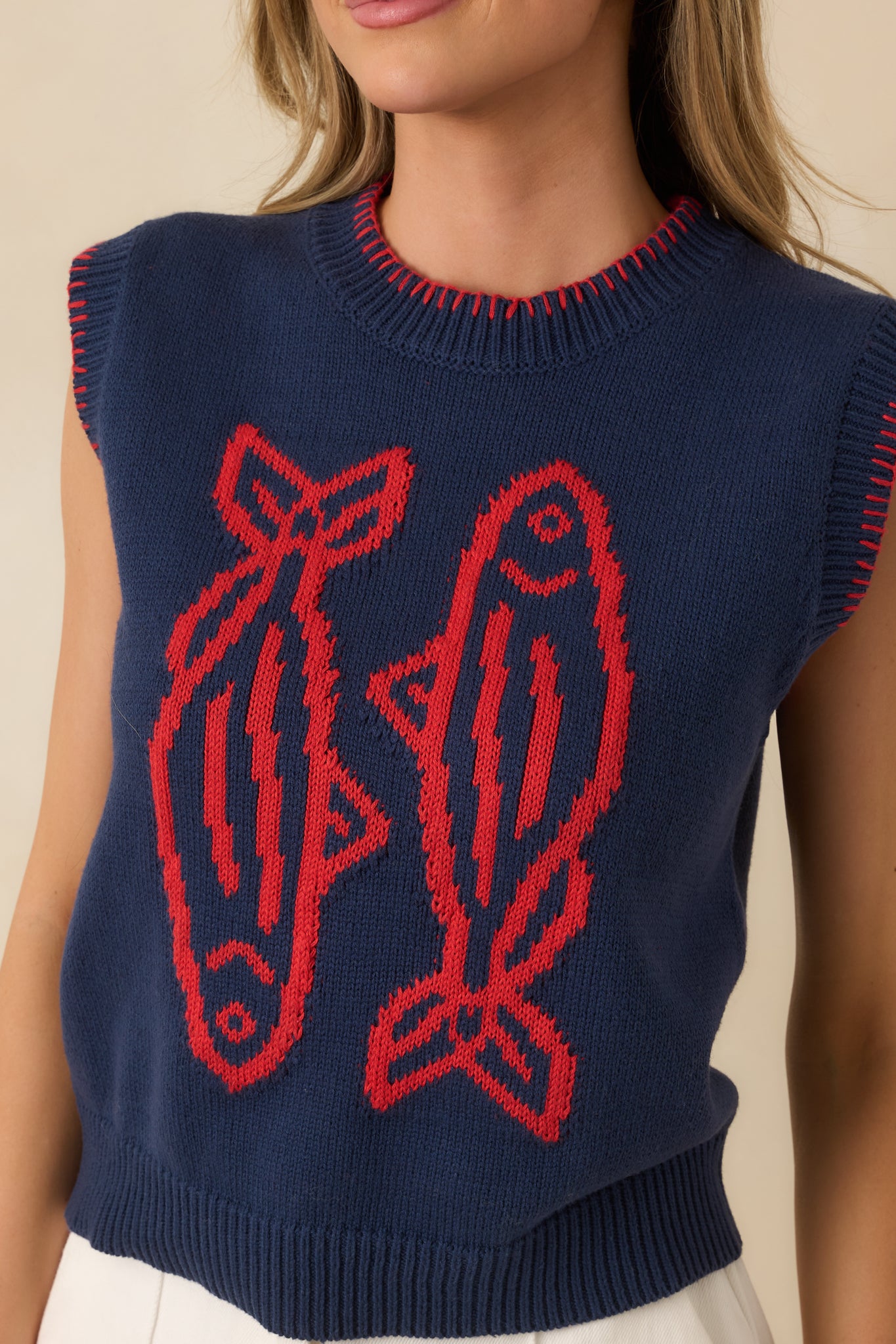 Detailed view of navy sweater vest showing the statement fish graphic, ribbed trim, and bold contrast stitching.