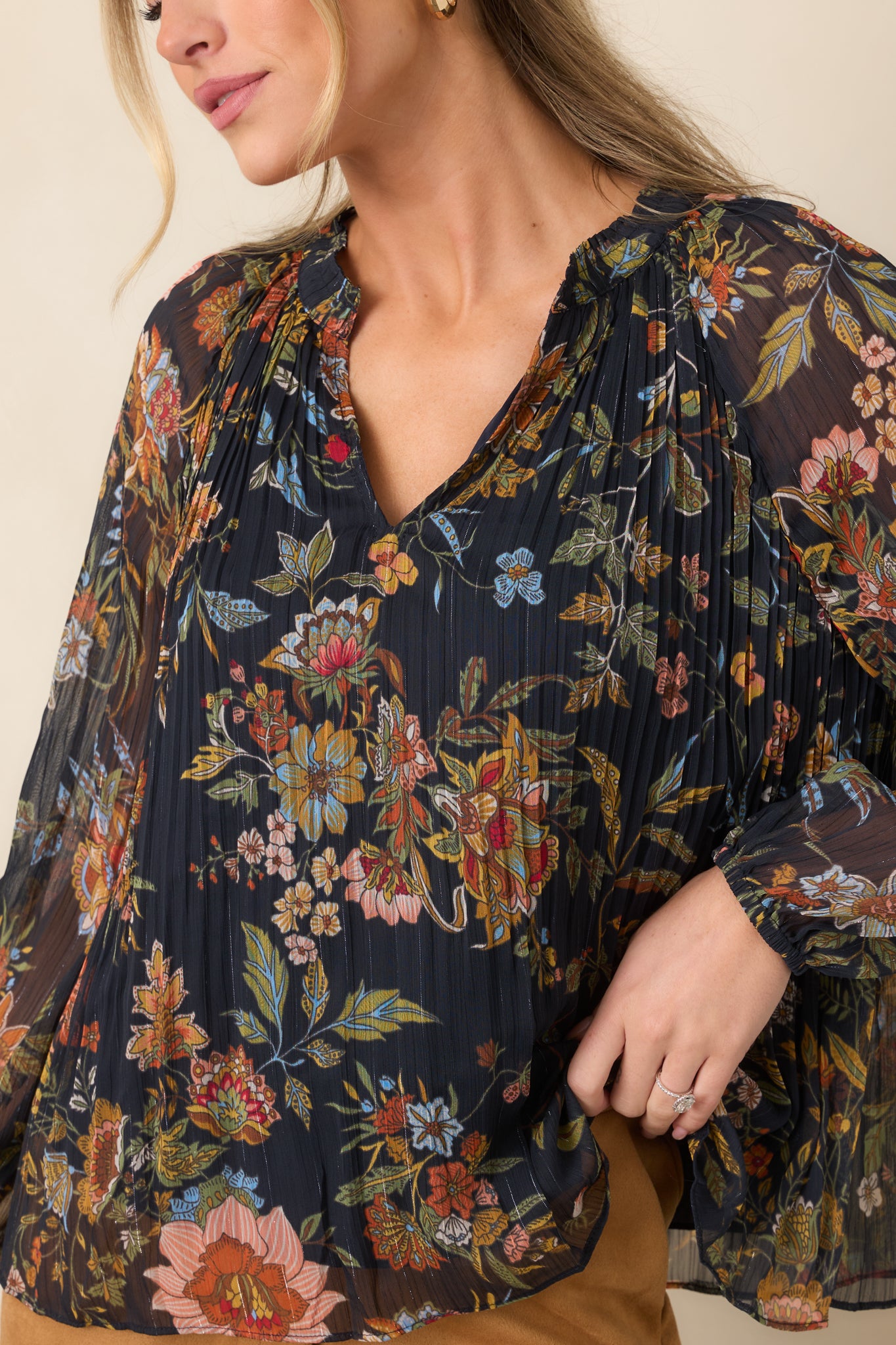 Close-up of the ruffled split V-neckline, fine pleating, and warm-toned botanical pattern on the navy top.