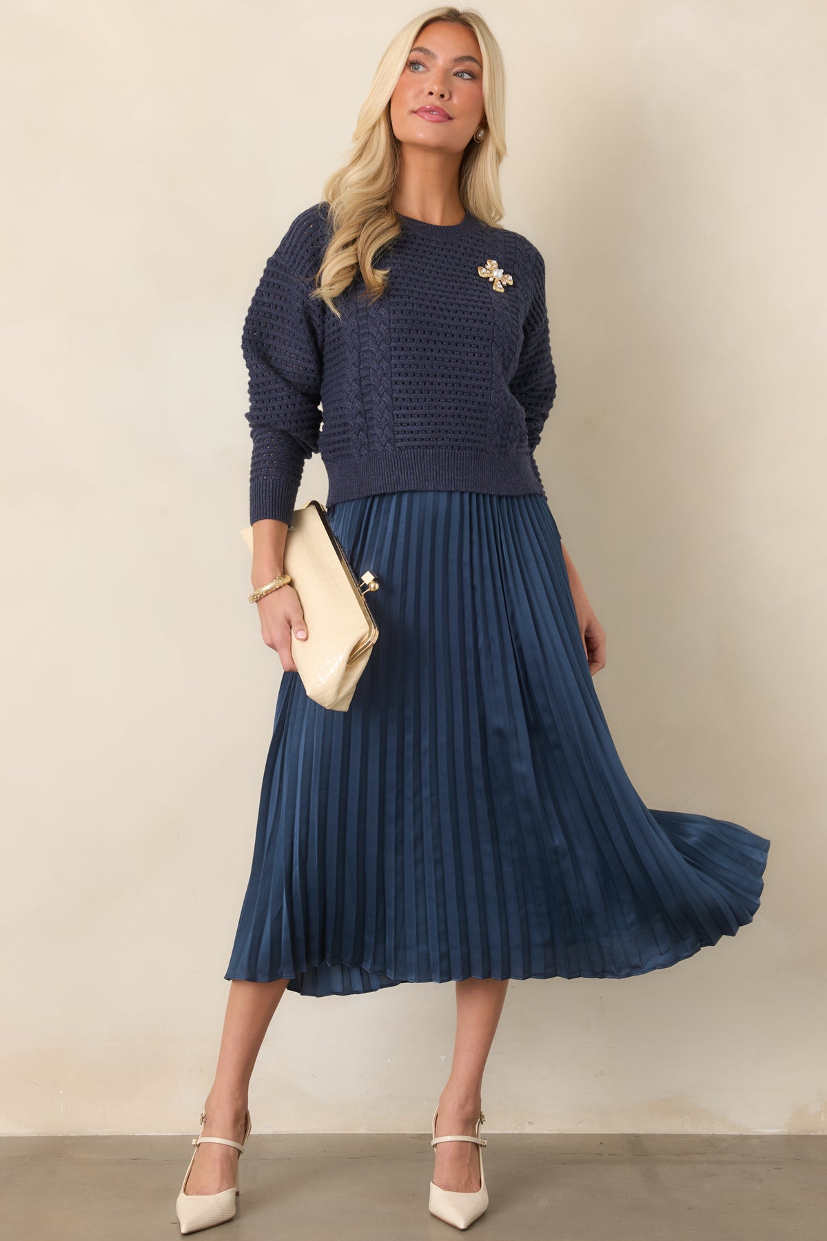 Navy two-piece set pairing a textured open-knit sweater with a sleeveless satin dress and pleated midi skirt.