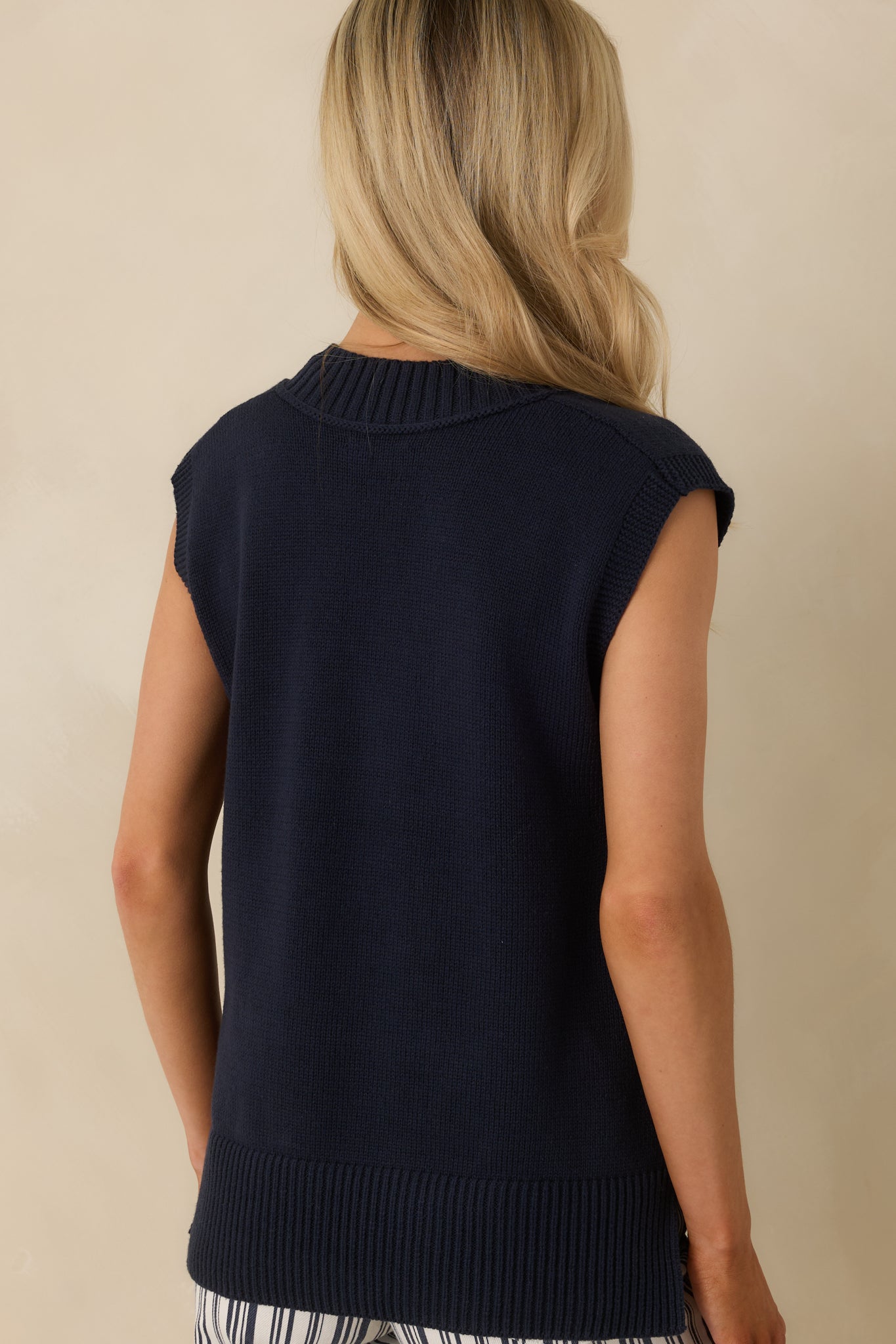 Navy knit vest displaying the relaxed silhouette from the rear with ribbed hem and arm openings for a clean, polished finish.