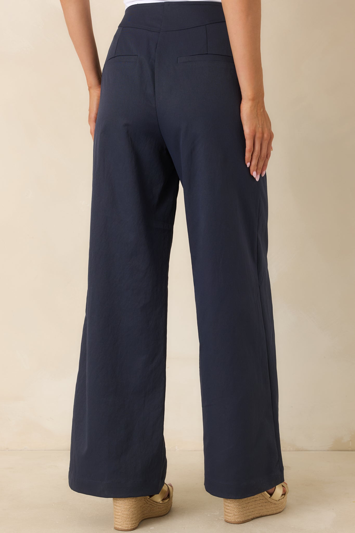 Back view of navy wide-leg pants showcasing welt pockets, smooth fabric, and elongated silhouette.