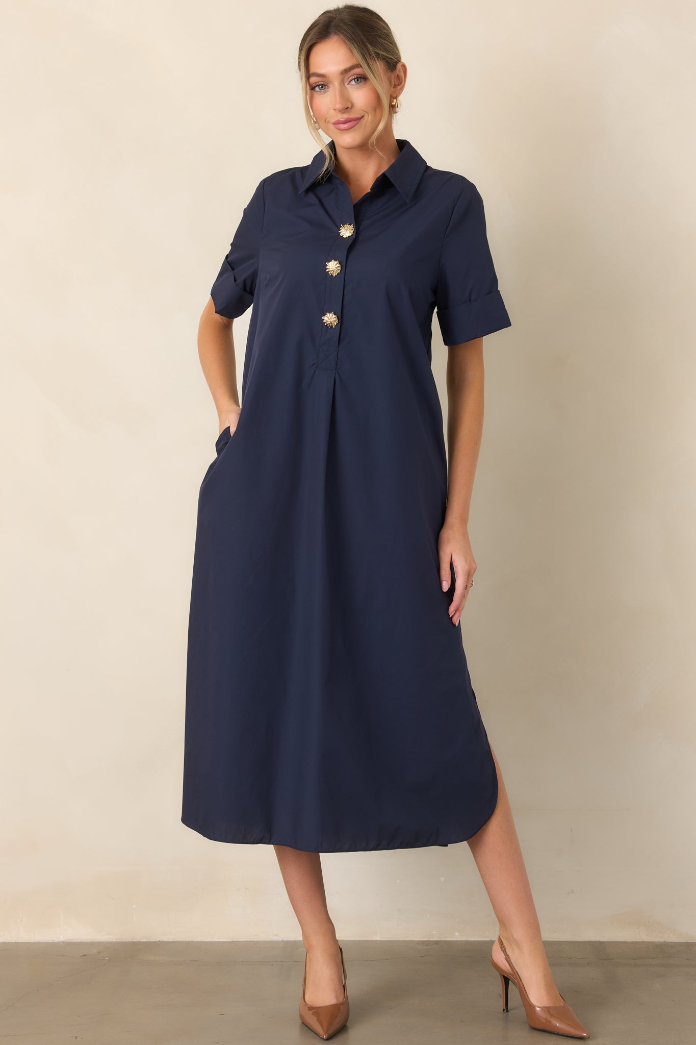 Navy woven maxi shirt dress highlighting its relaxed fit, rolled short sleeves, side pockets, and elegant gold floral buttons.