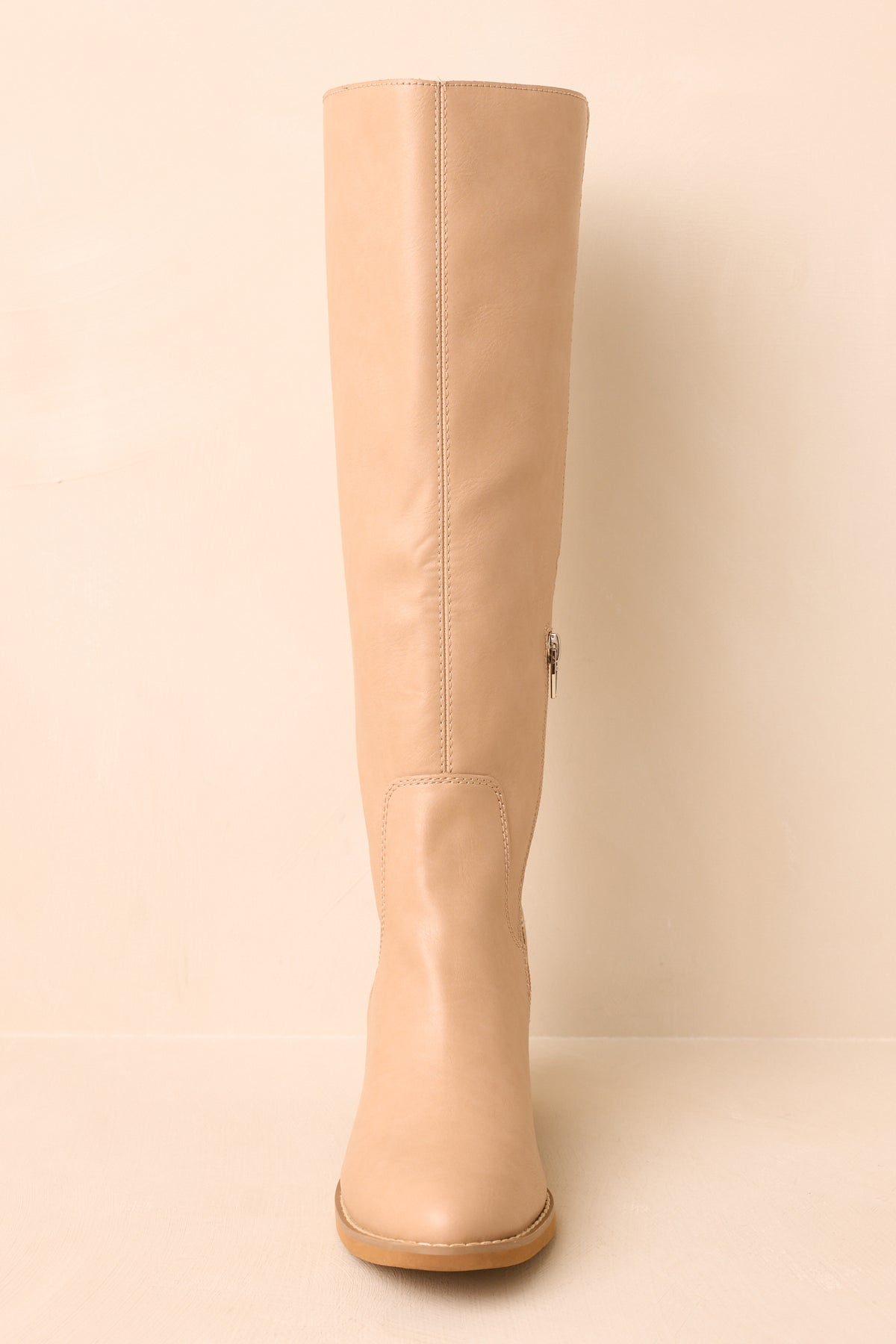Neutral knee-high boots highlighting the softly rounded almond toe, smooth shaft, and structured stacked heel.