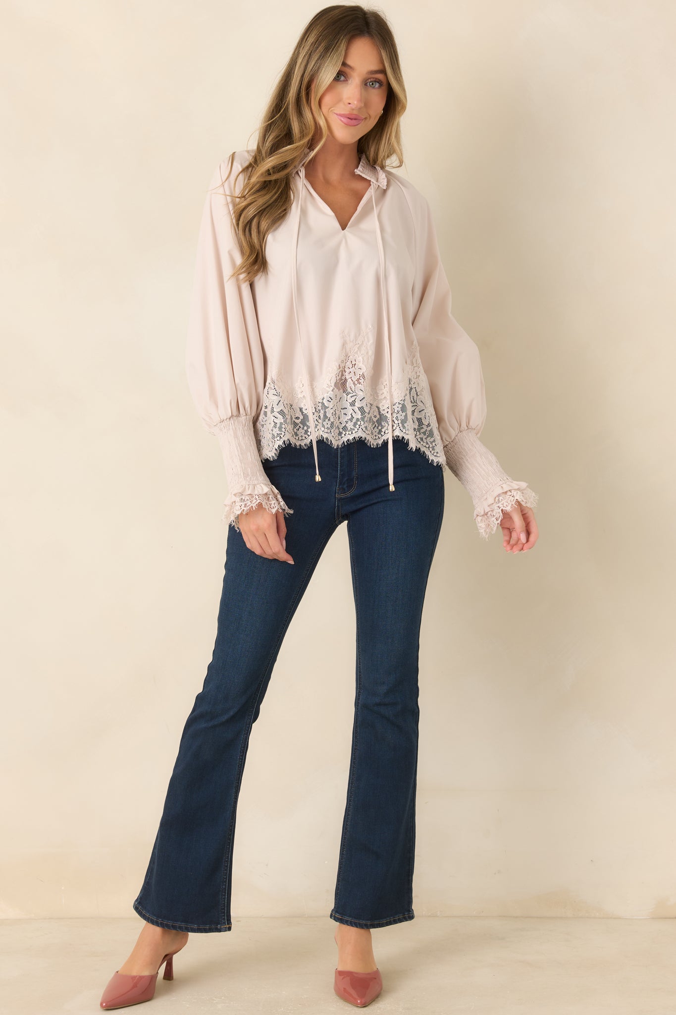 Relaxed woven blouse in a soft neutral shade showcasing a ruffled neckline with flowing ties, voluminous balloon sleeves, smocked cuffs with lace accents, and a floral lace hem.