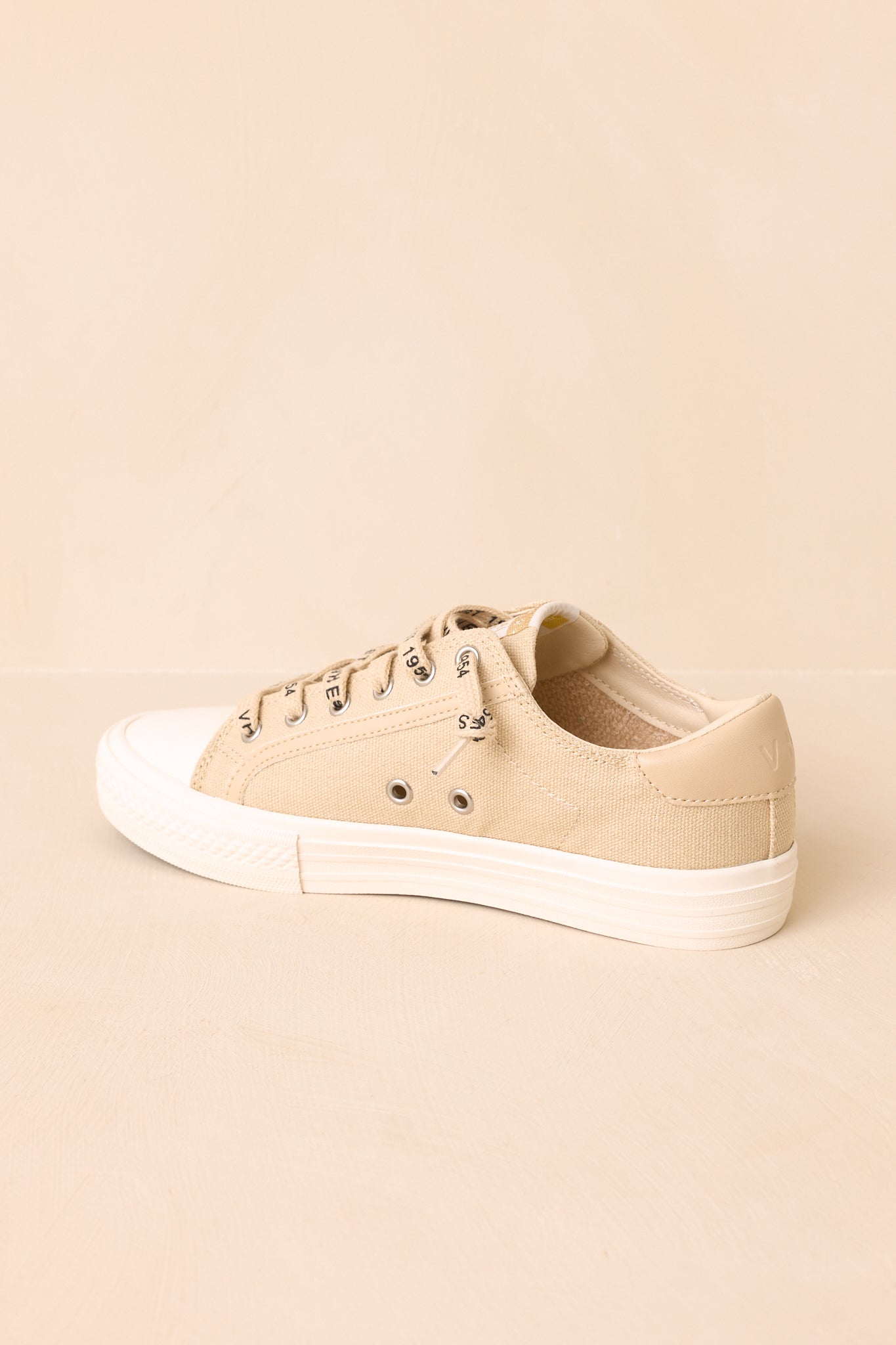 Nude canvas sneakers with playful retro-inspired faux leather accents and branded lace-up closures displayed from an alternate angle on a beige background.