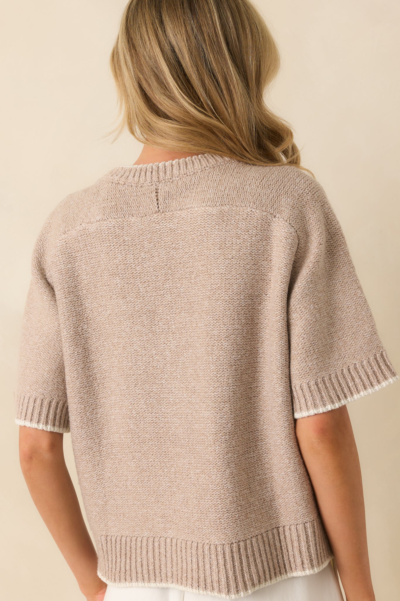 Rear view of the oatmeal beige sweater, showing the oversized fit, short sleeves, ribbed hem, and contrast trim.