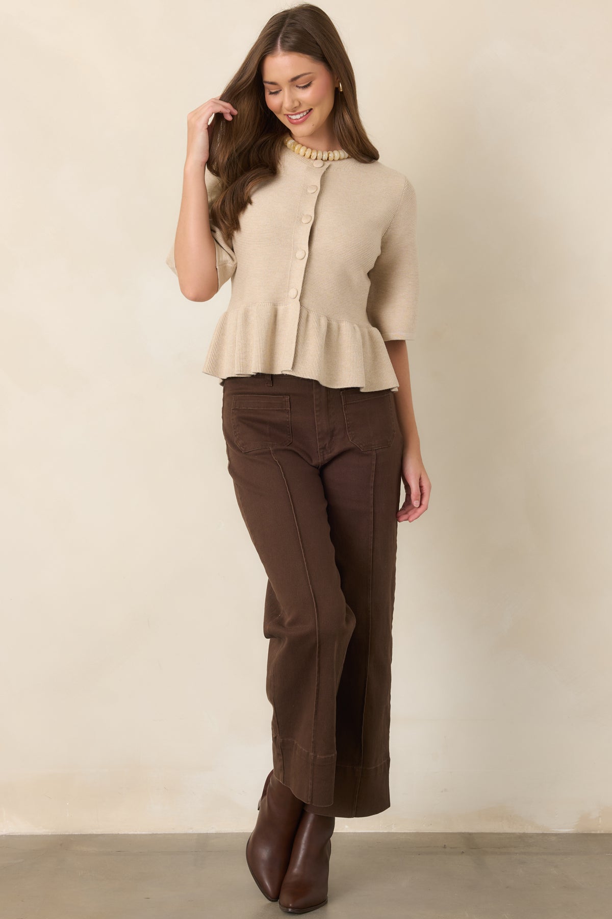 Smooth oatmeal knit top with a feminine fitted shape, round neck, covered button-front detailing, elbow-length sleeves, and subtle waist-defining peplum.