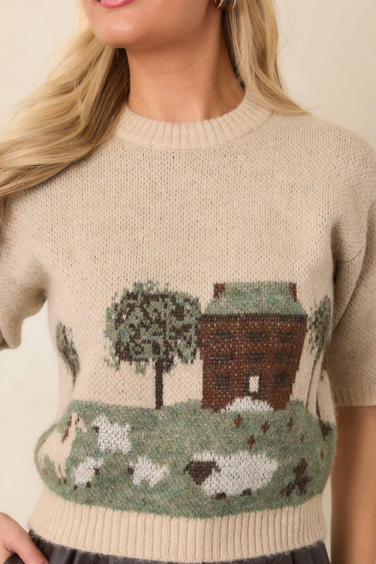 Close-up of the scenic intarsia design showing grazing sheep, leafy trees, and a quaint cottage against the oatmeal knit.