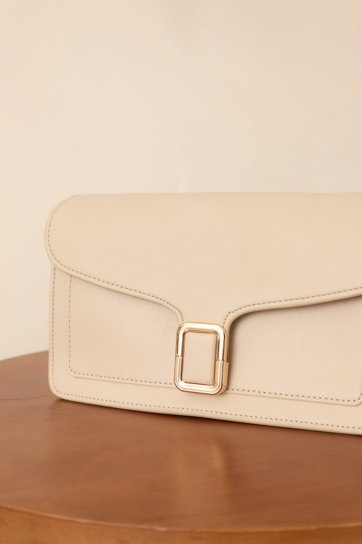 Off-white handbag showcasing tonal edge stitching, a sculpted envelope flap, gold-tone buckle clasp, and matching strap hardware.