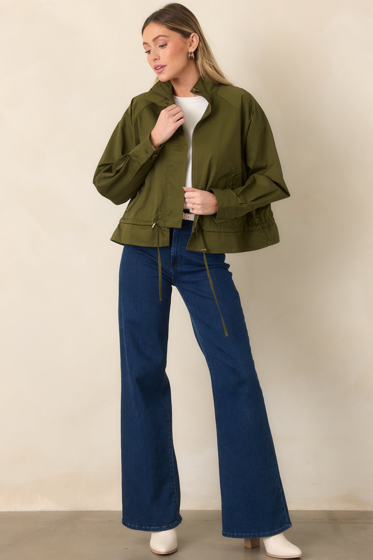 Olive cotton jacket with a stand collar, zip front, snap accents, and softly ruffled hem.