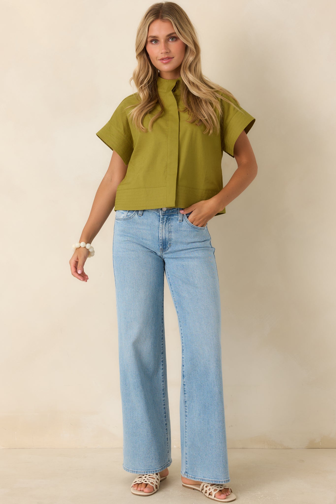 Olive green cotton linen top featuring a modern mock neckline, concealed button-front placket, cuffed short sleeves, and a cropped silhouette.