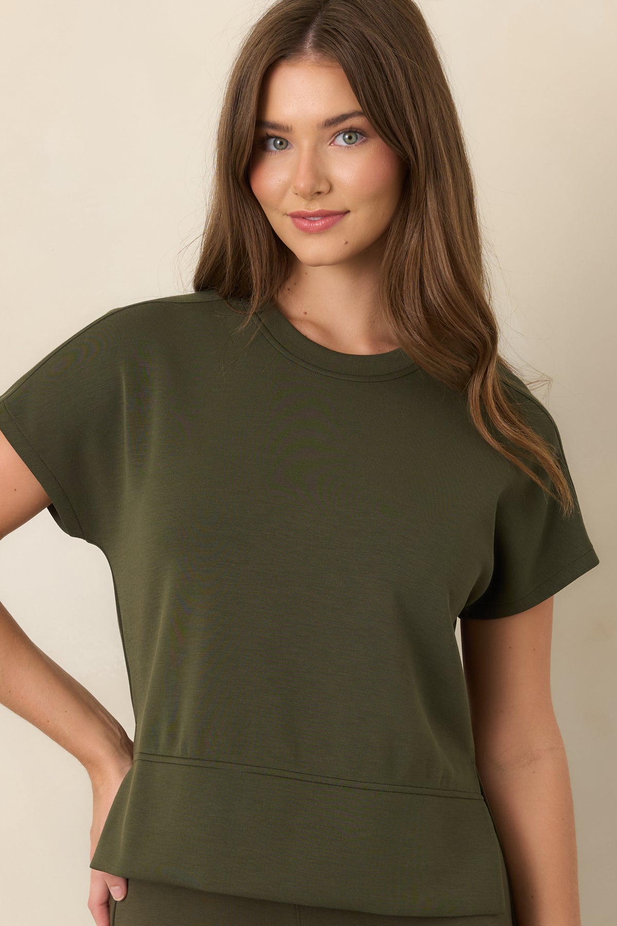 Close view of the olive-green top highlighting the classic crew neckline, smooth spacer fabric, and short sleeves.