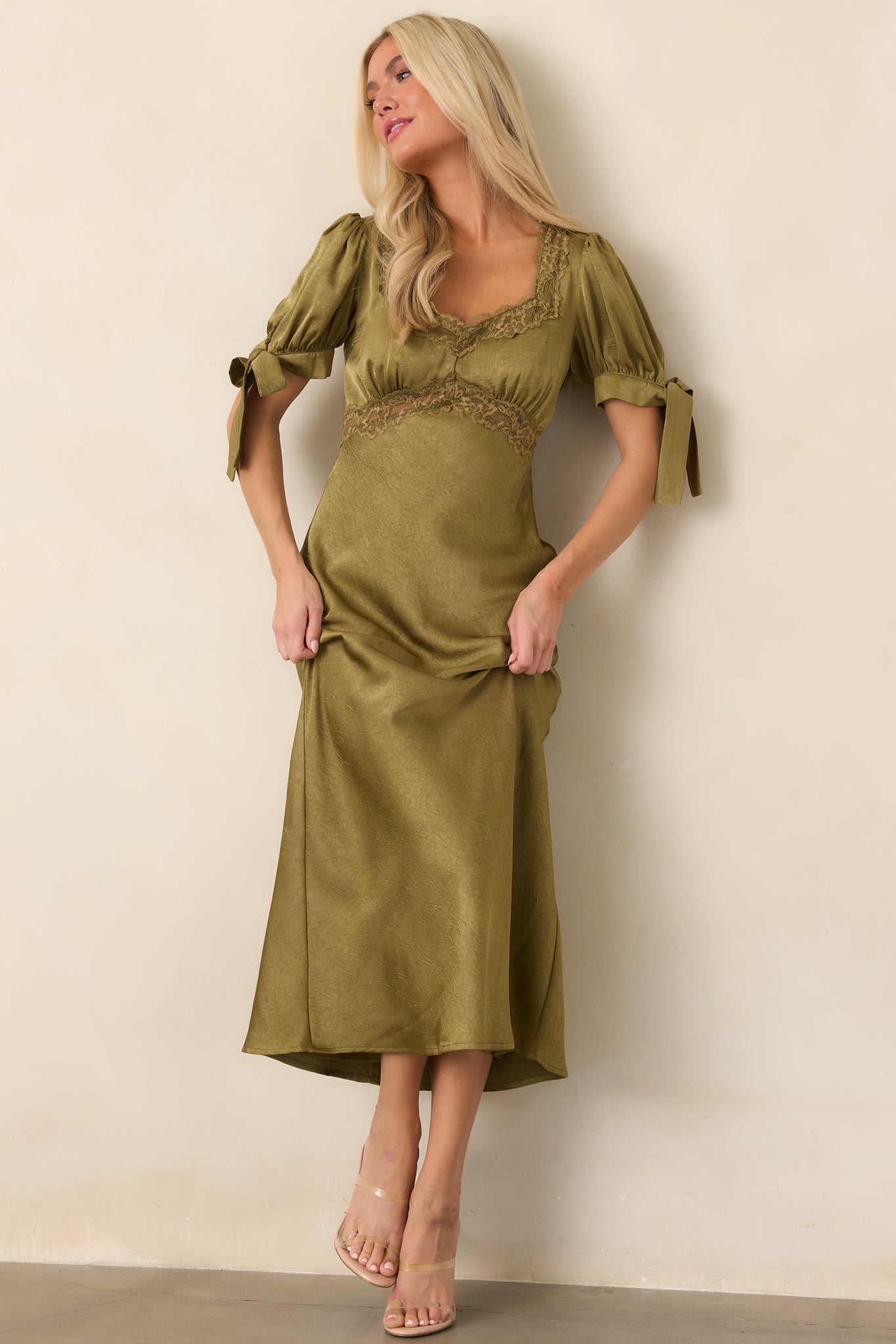 Lustrous olive green satin midi dress featuring a lace-trimmed neckline, short puff sleeves, empire waist, and fluid flowing skirt.
