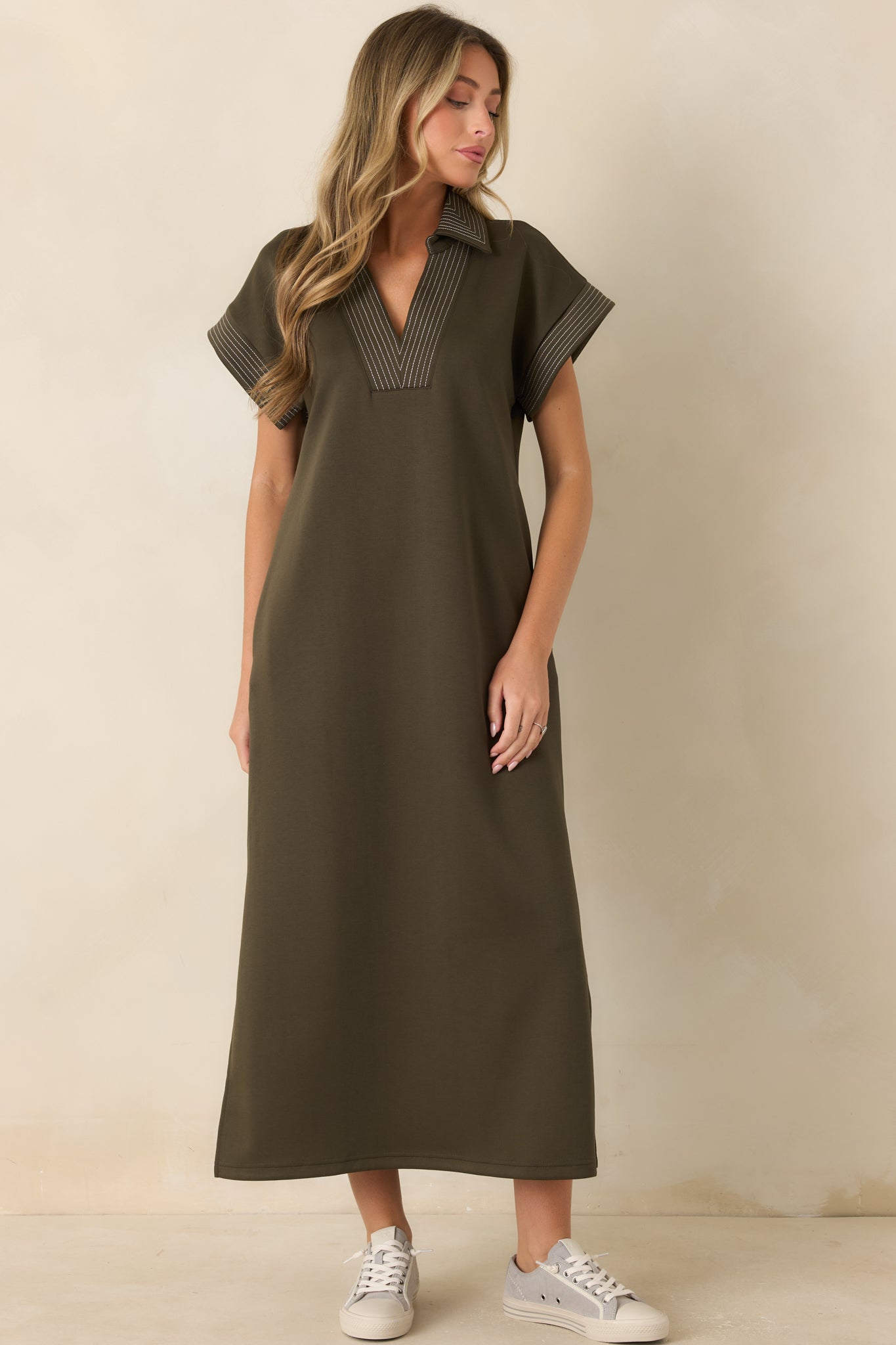 Olive hued knit dress featuring pinstriped edging, side pockets, and a flowing maxi length design with comfortable movement.
