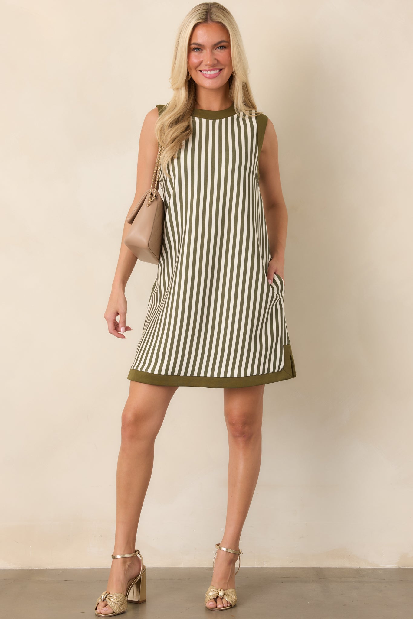 Olive and ivory vertically striped mini dress with a round neckline, contrast olive trim, sleeveless design, and relaxed straight silhouette.