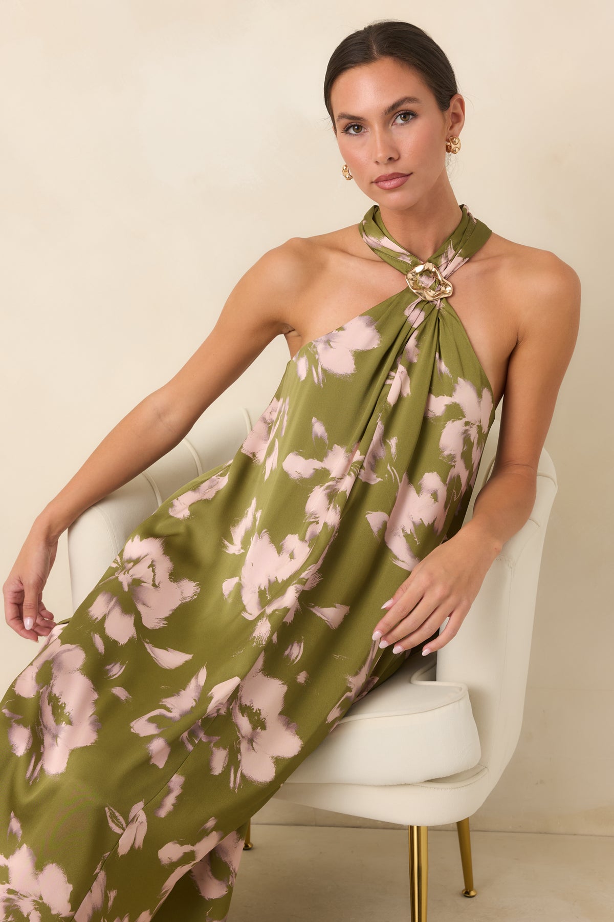 Olive maxi dress with painterly blush blooms, sculptural gold-tone halter accent, and flowing sleeveless silhouette.