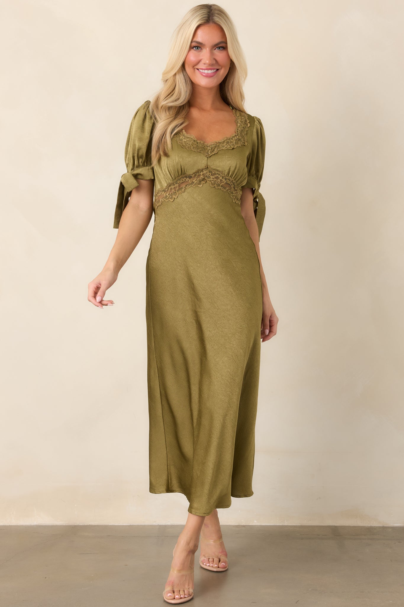 Flowing olive green satin dress with a feminine empire silhouette, short puff sleeves, and delicate lace accents along the bodice.