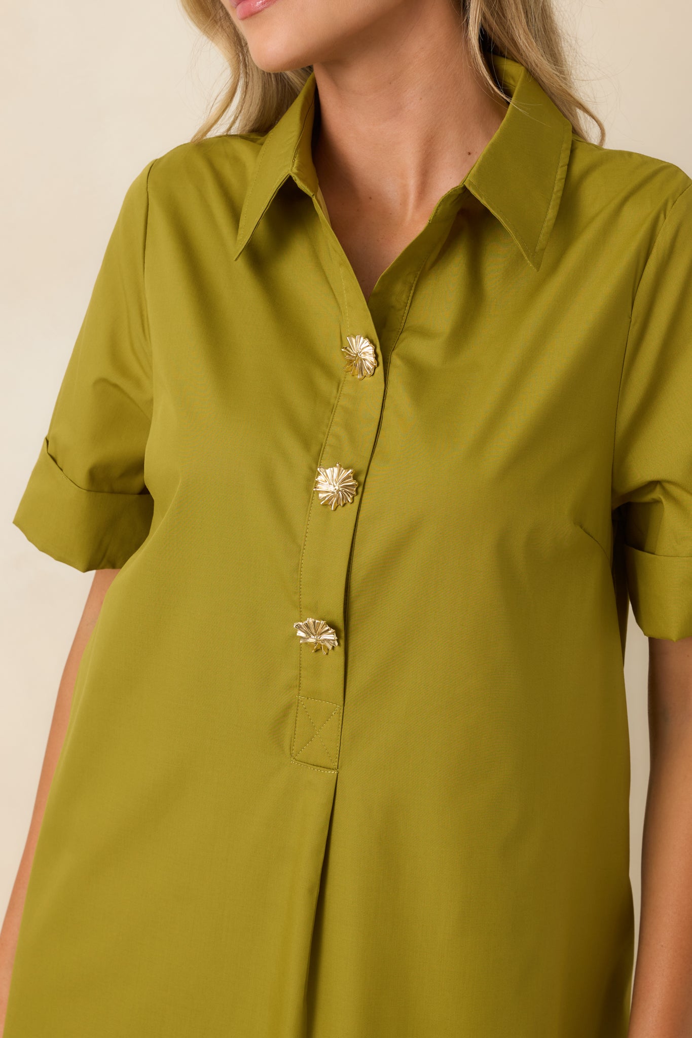 Close-up of the olive woven fabric highlighting the gold floral buttons, collared neckline, and refined shirt dress details.