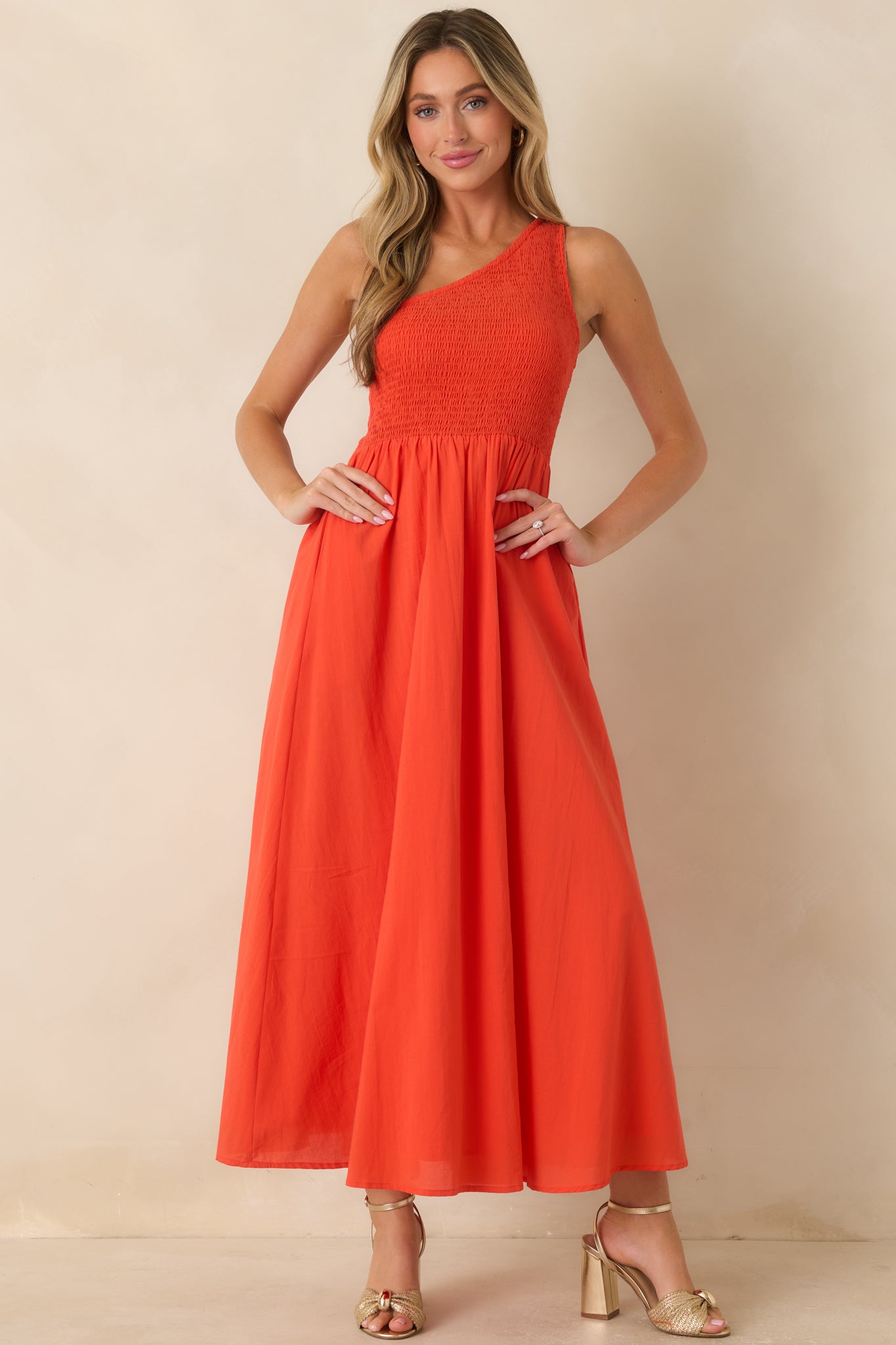 One-shoulder coral-orange maxi dress with a fully smocked bodice, flowing A-line skirt, and breathable cotton fabric for effortless movement