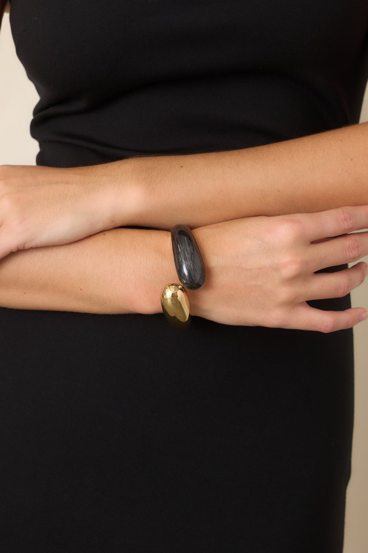 Open cuff bracelet featuring a polished gold-tone end and rounded black marbled end.