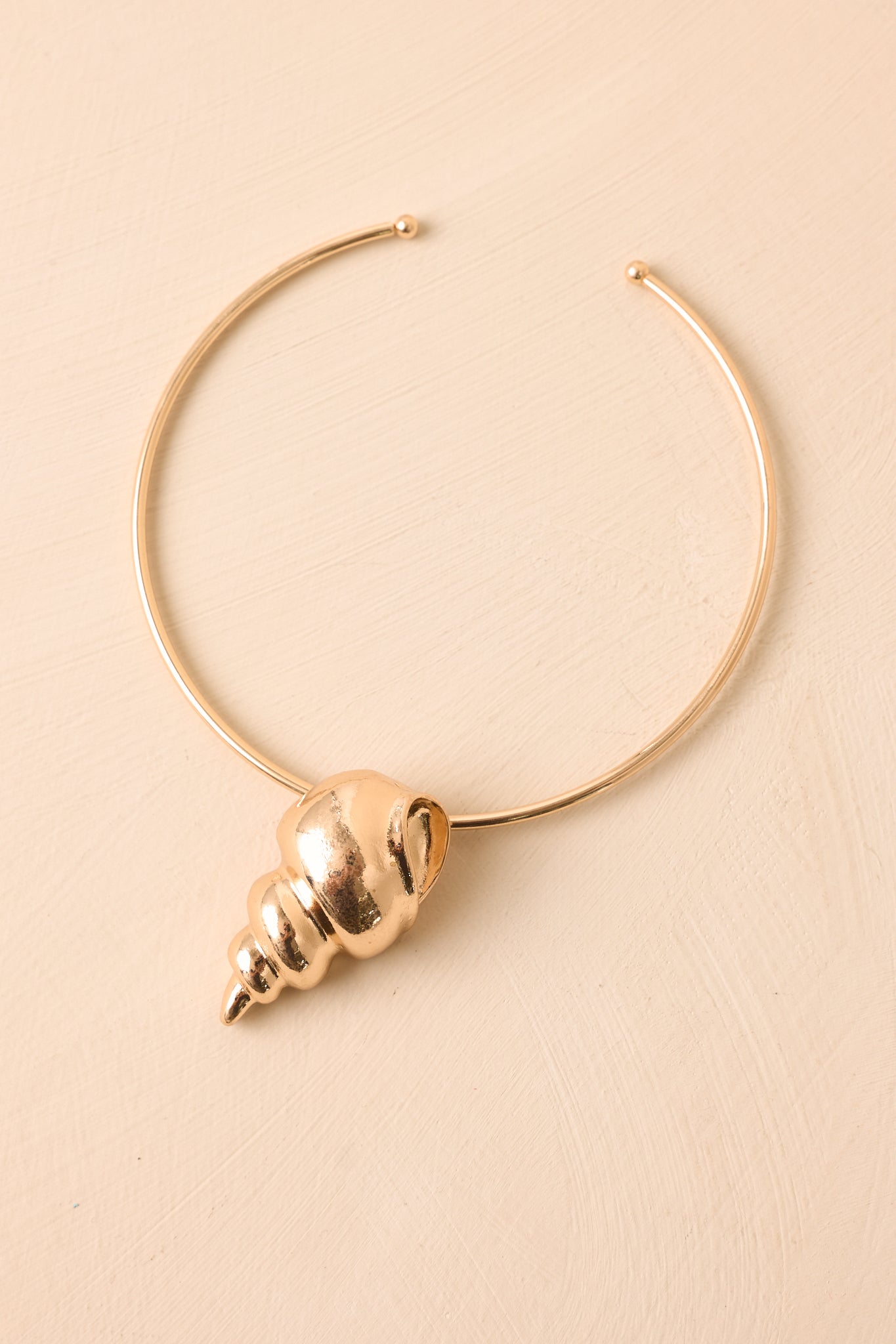 Angled view of structured gold necklace on beige backdrop emphasizing sculptural shape and shine.