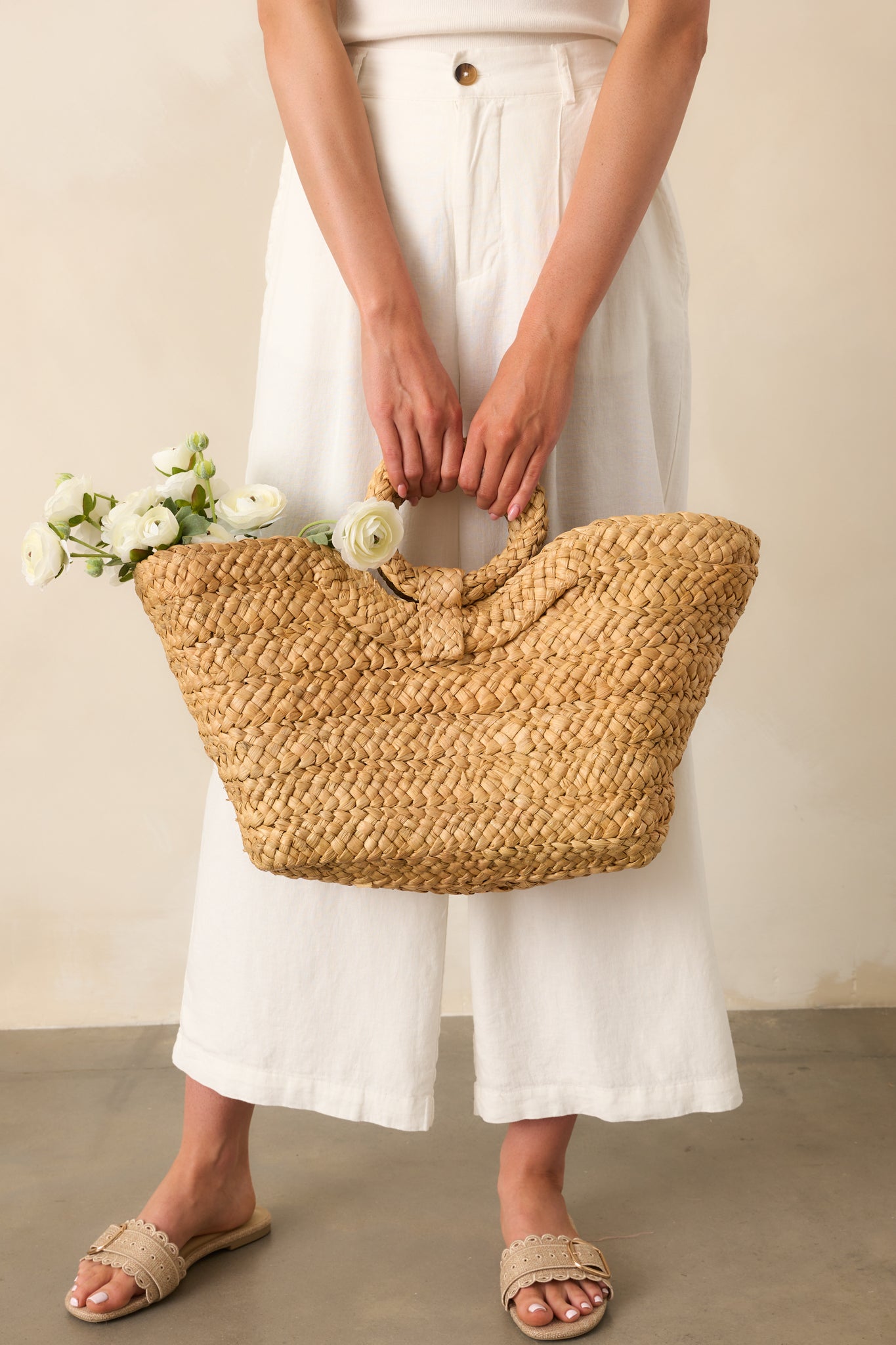 Full view of the open tote handbag carried by hand, showcasing the circular woven handles and tan raffia exterior.